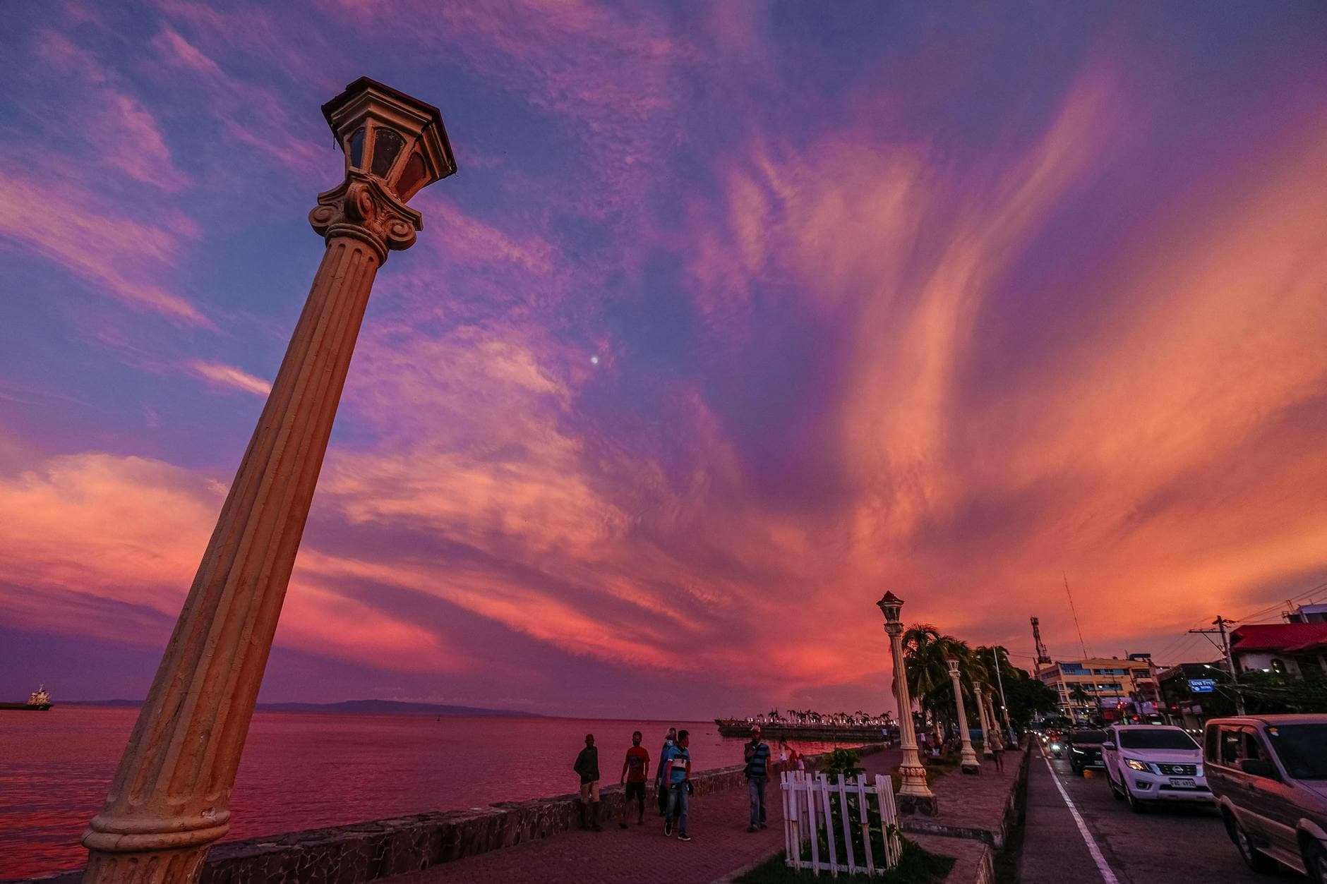 Captivating sunset over a seaside city walkway with stunning skyscape and urban lights.