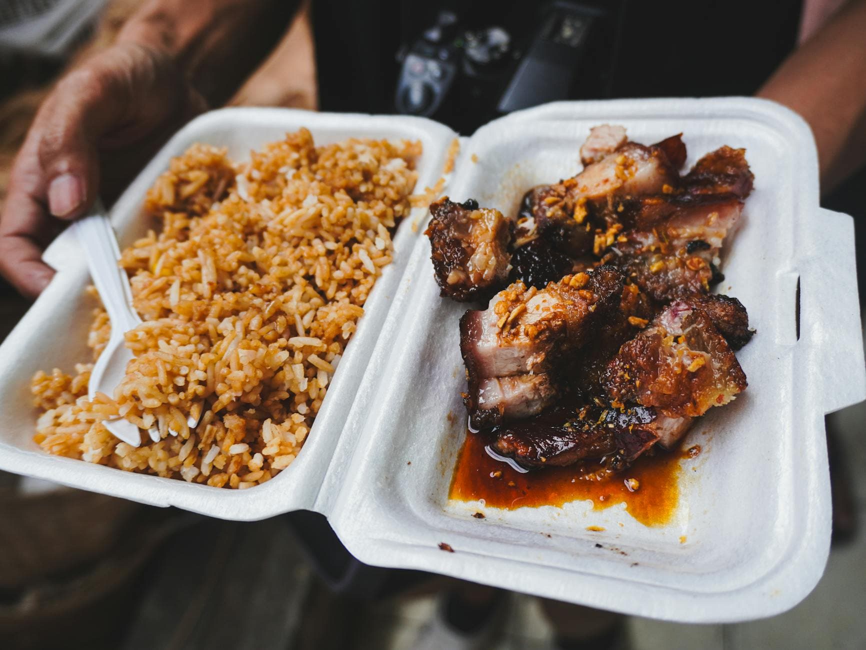 A close-up of Filipino street food with fried rice and grilled pork in a takeout container.