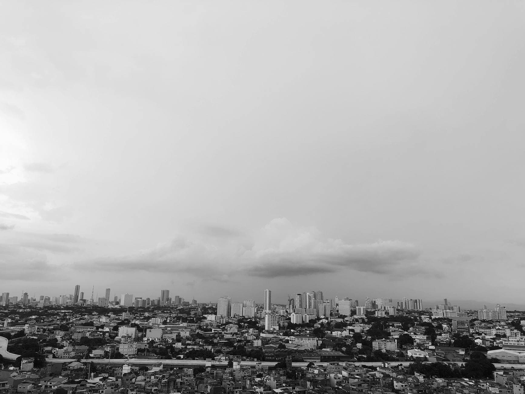 A captivating grayscale aerial view of Manila's urban skyline with cloud-filled skies.