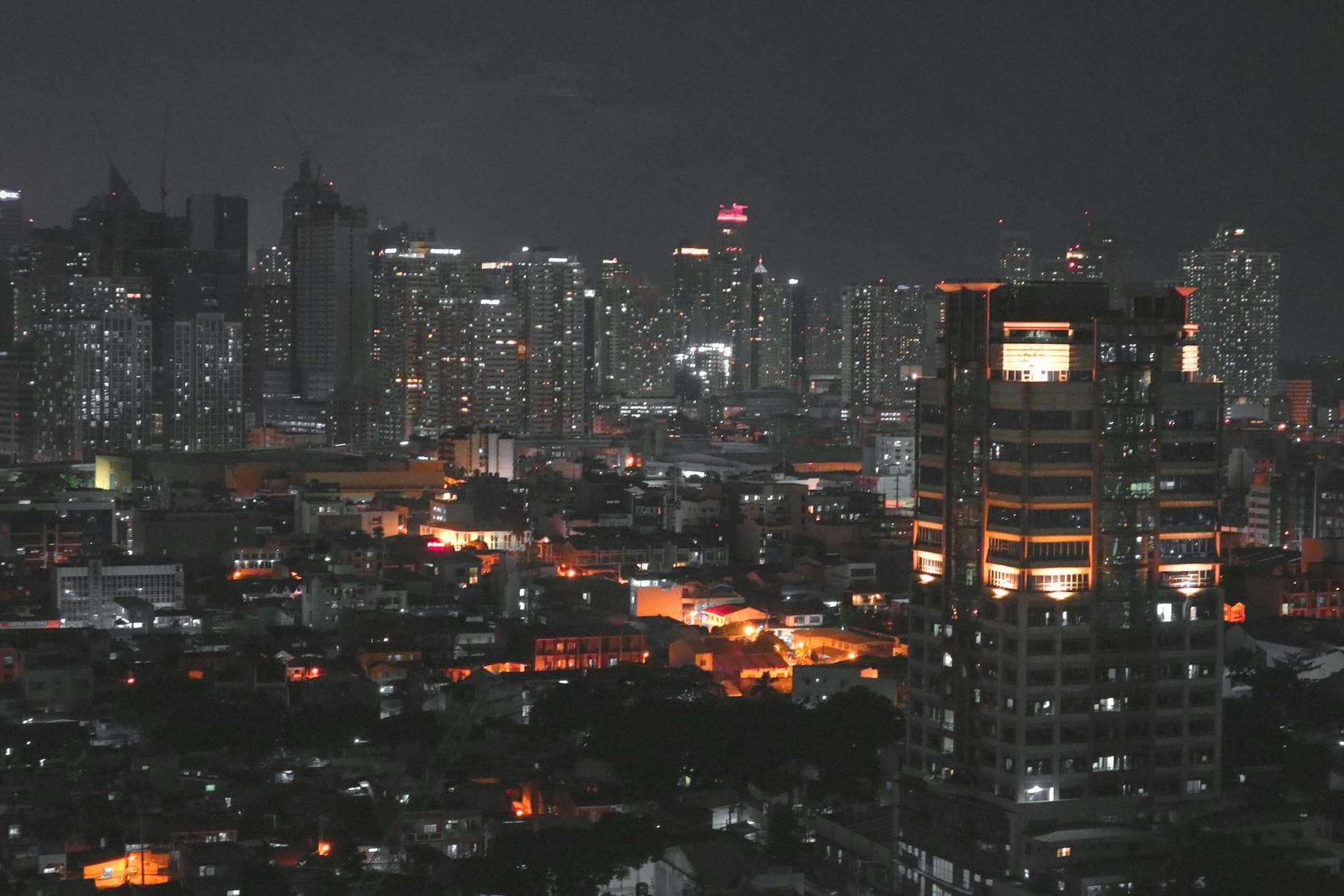 A stunning aerial view of Manila cityscape at night featuring brightly lit skyscrapers and urban glow.