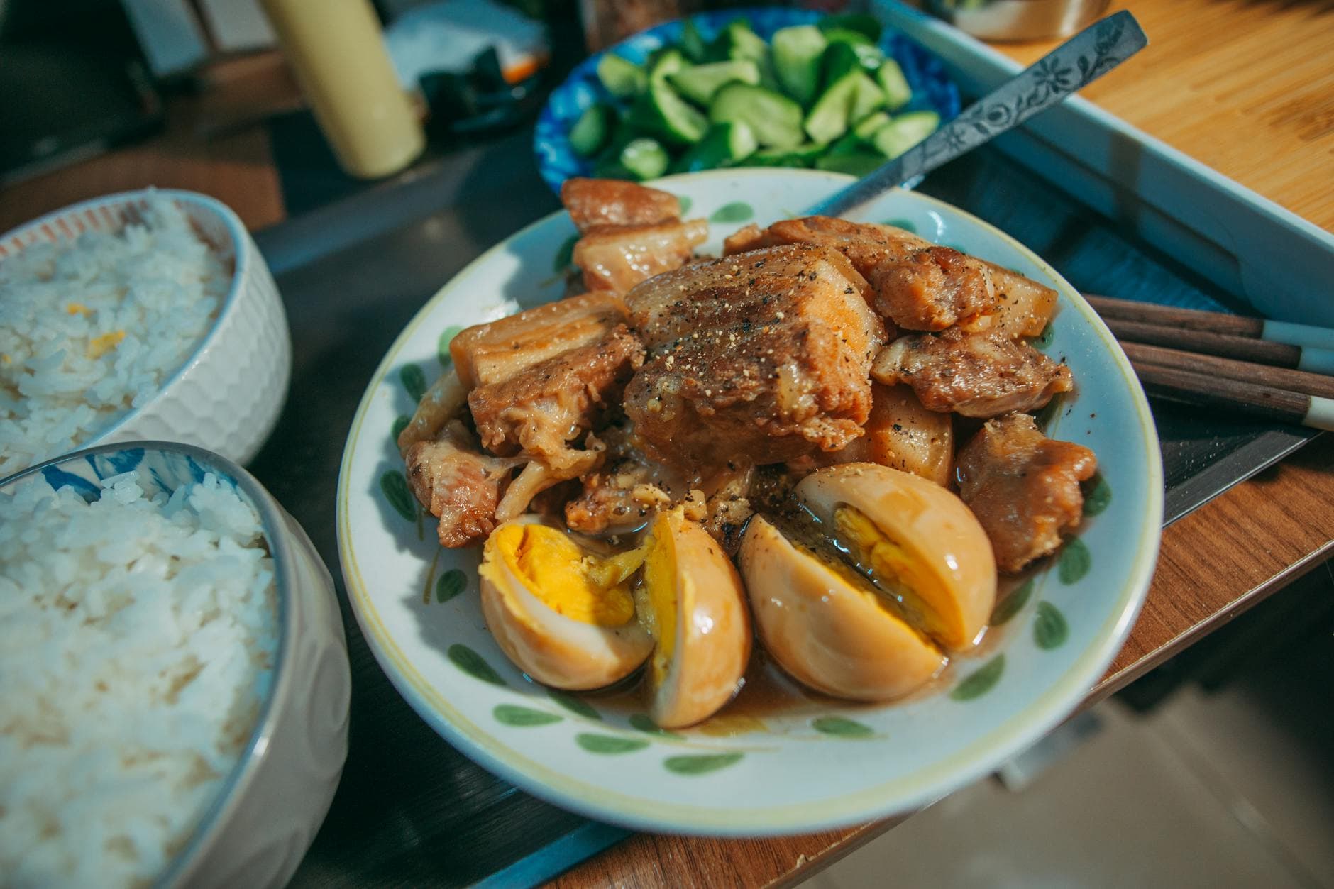 A plate of Filipino pork adobo with boiled eggs served alongside rice and fresh vegetables.