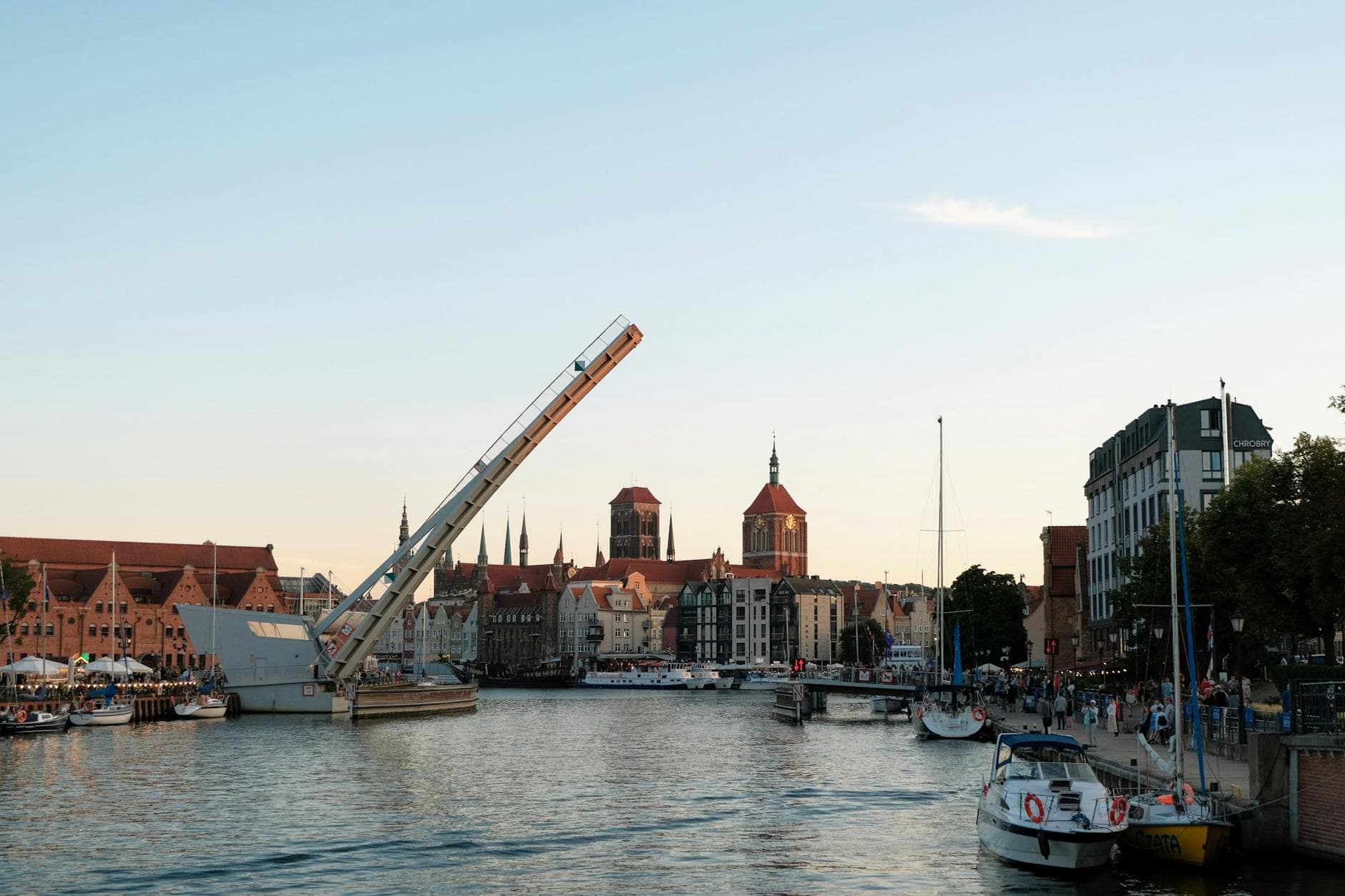 Scenic view of the Gdańsk waterfront featuring a raised bridge against a sunset sky.