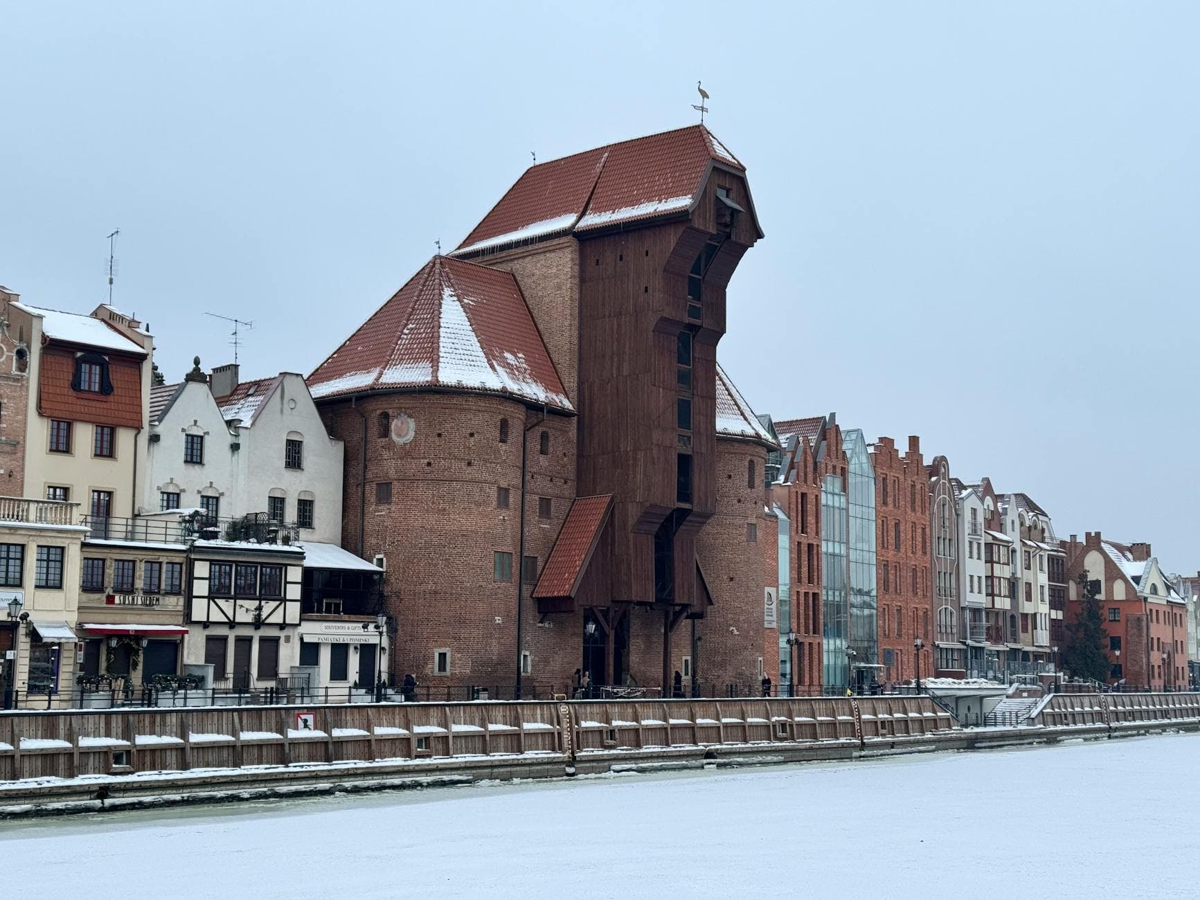 The iconic Gdansk Crane, a historic landmark, covered in winter snow along the river.