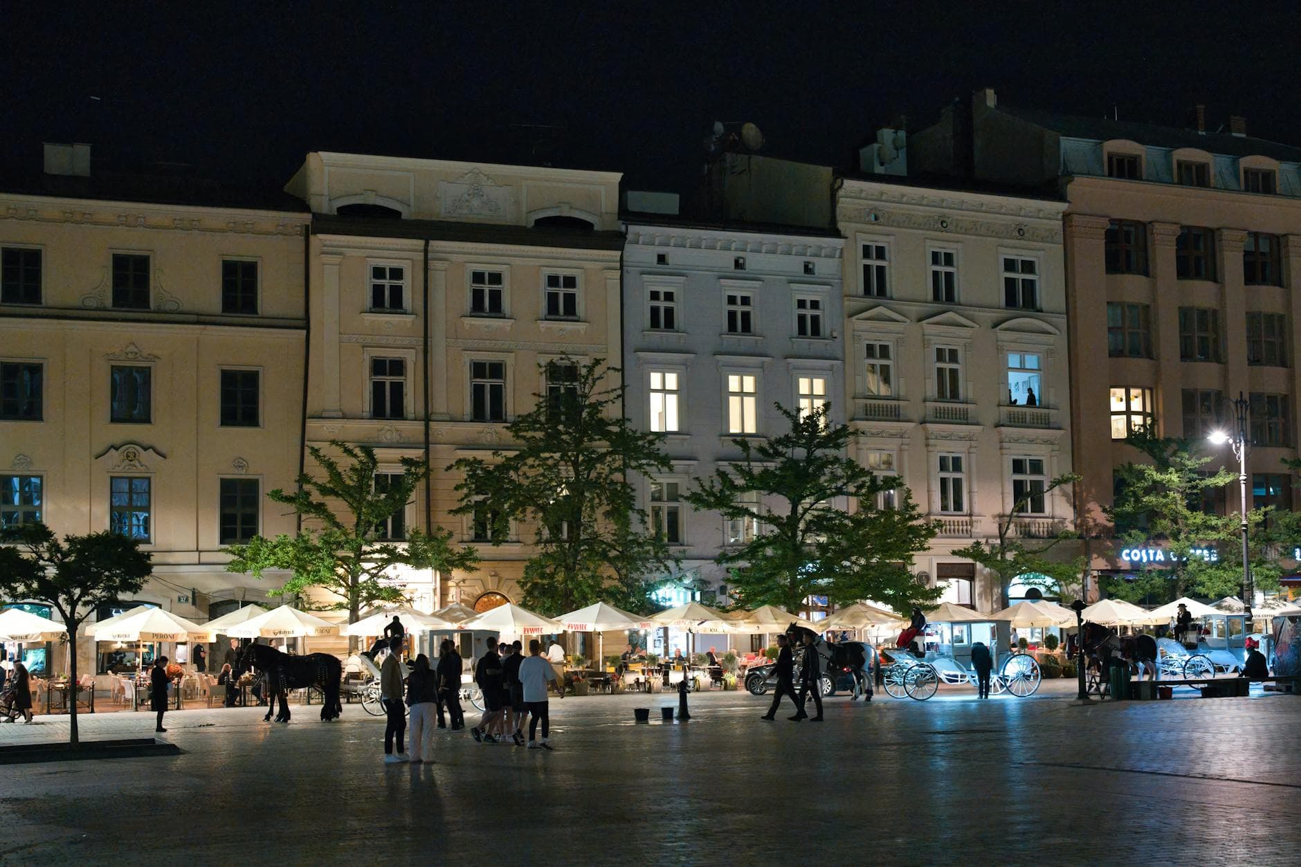 Illuminated city square in Kraków at night, showcasing historic architecture and lively atmosphere.