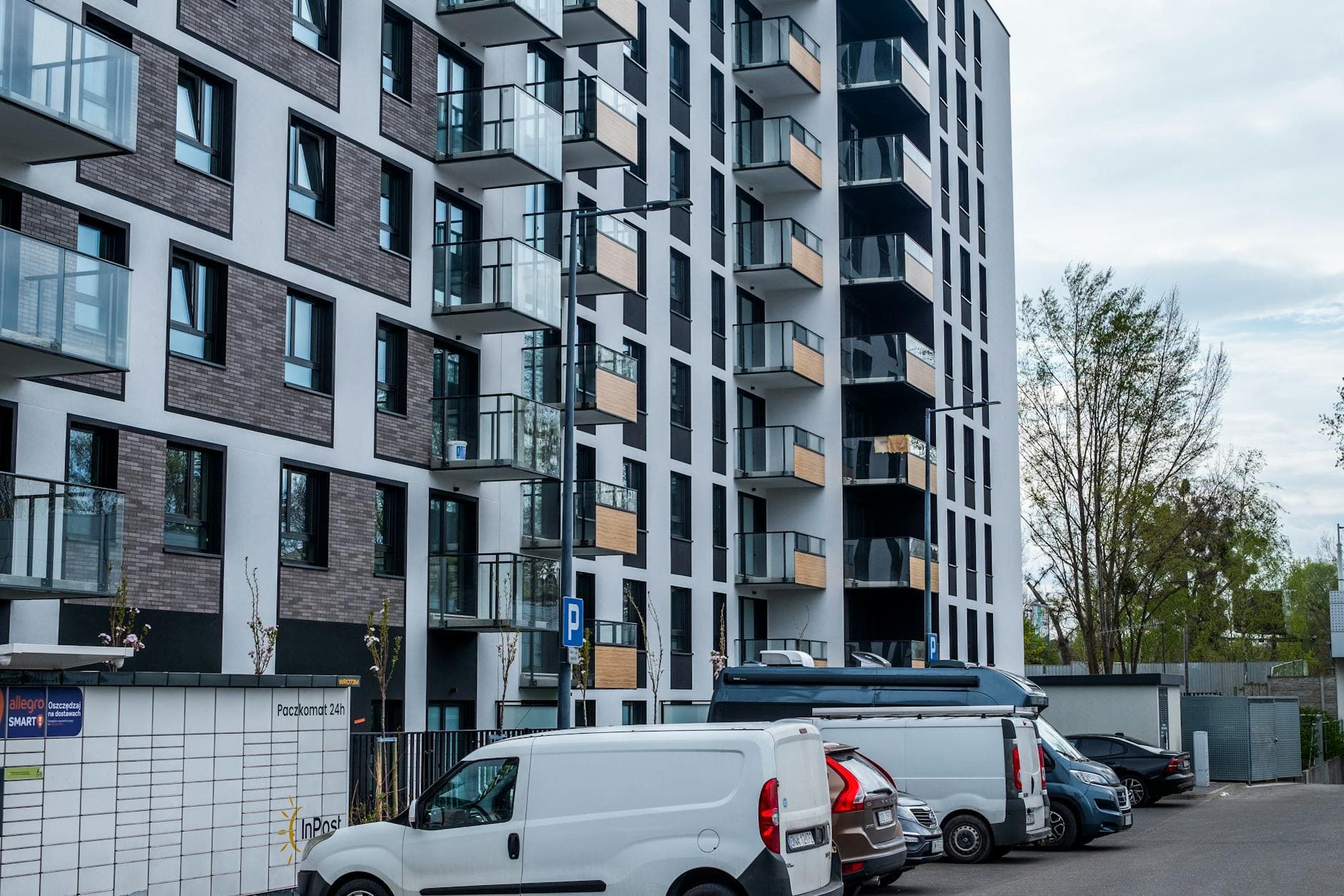 Contemporary apartment building with parking area and vehicles in a city setting.