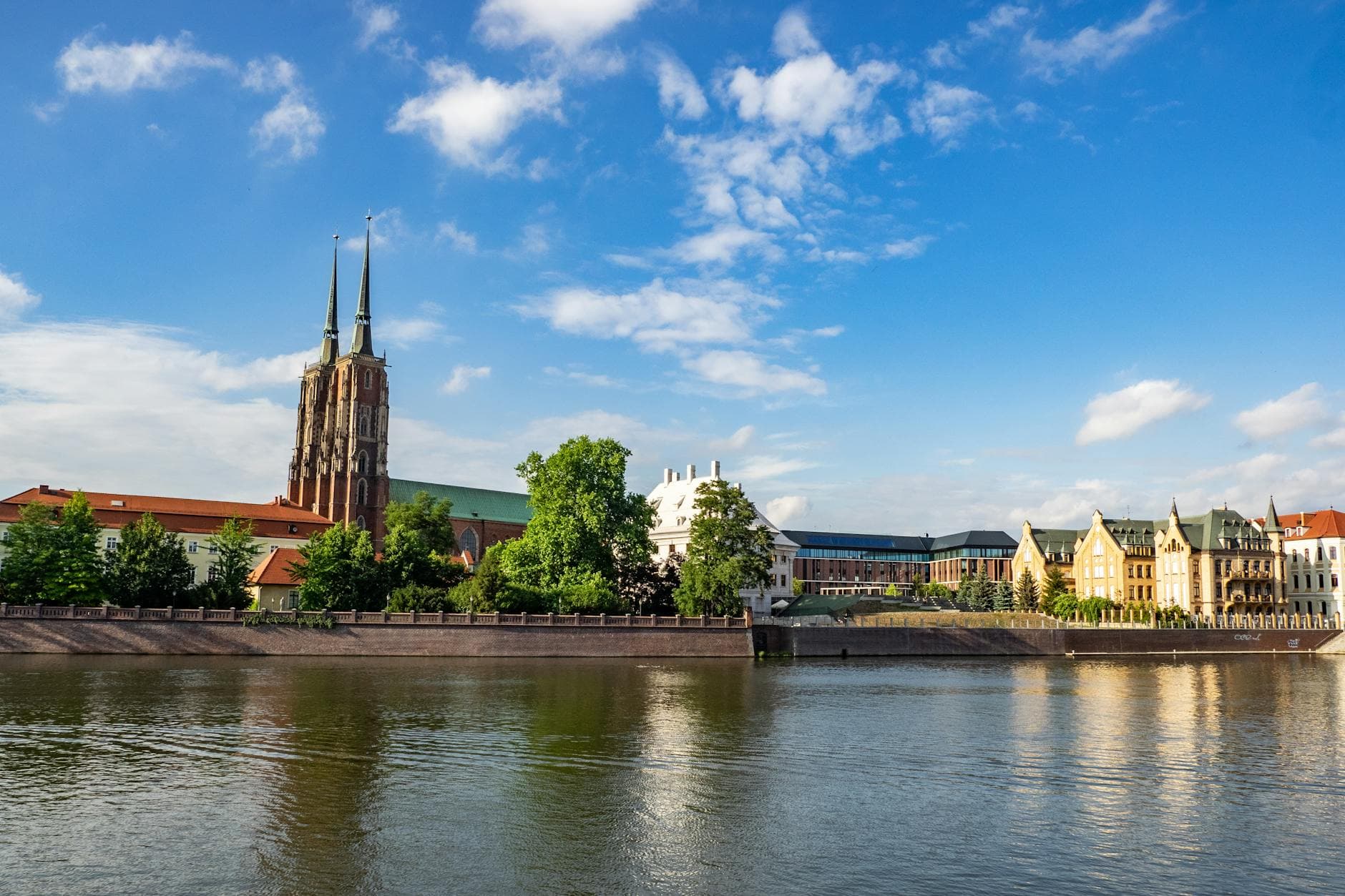 Scenic view of Wrocław Cathedral along the Oder River under a bright blue sky.