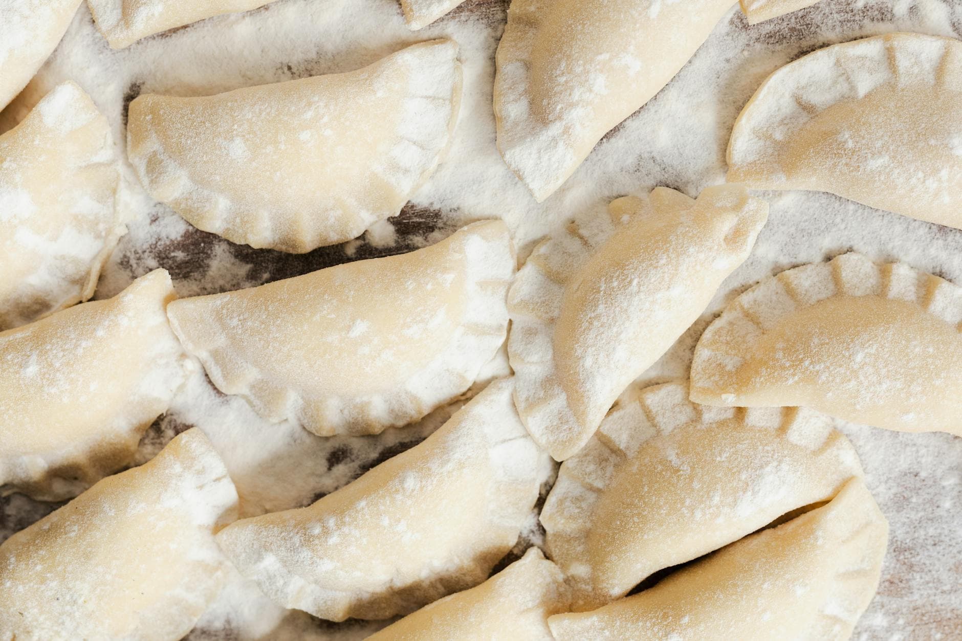 Top view of uncooked pierogi dumplings arranged on a floured surface, ready to cook.