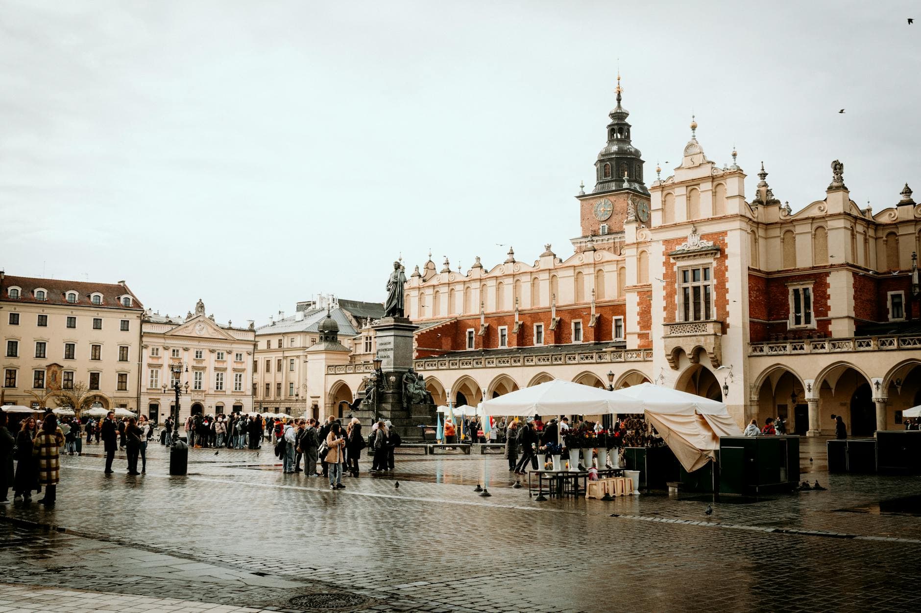 Bustling scene at Kraków's historic Market Square with Cloth Hall and statue.