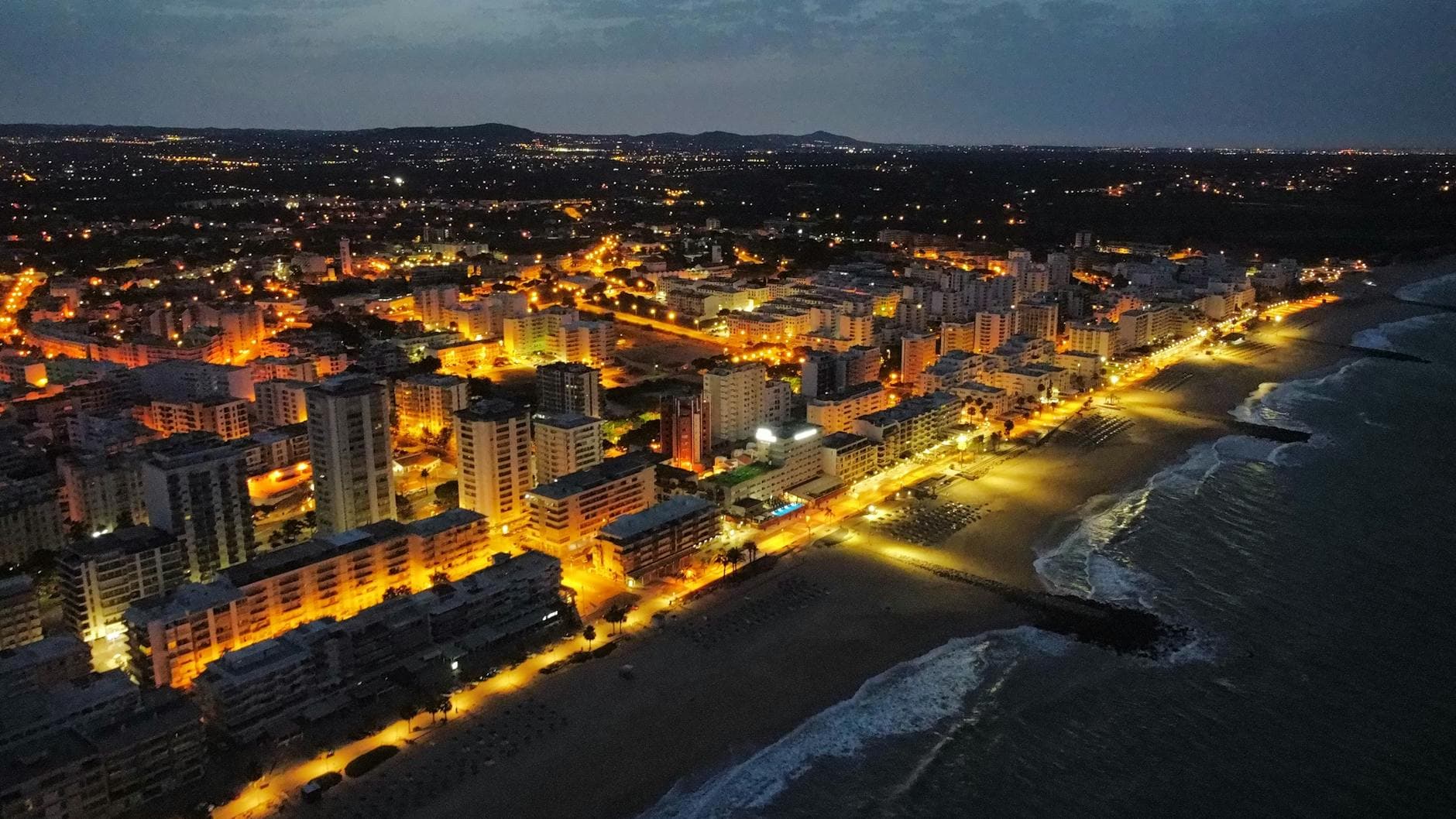A captivating aerial view of Faro, Portugal, showing the illuminated coastline at night.