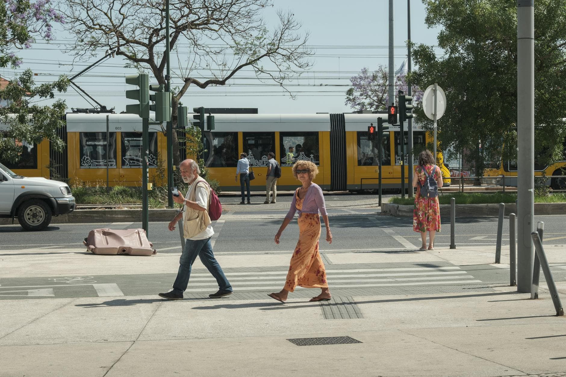 Street scene in Lisbon with pedestrians crossing in front of a yellow tram on a sunny day.