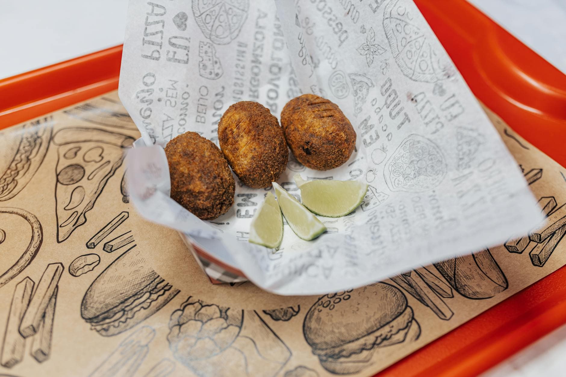 Crispy fried croquettes served with lime wedges on a decorative tray, perfect for fast food lovers.