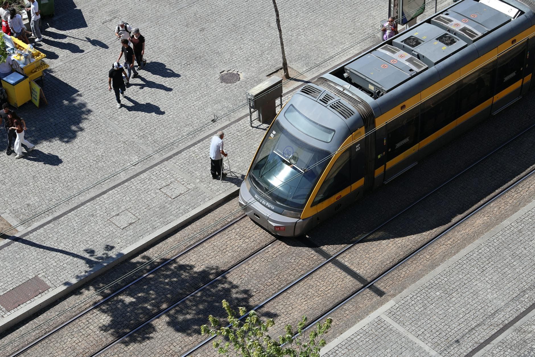 A bird's-eye view of a modern tram on tracks in Porto, Portugal with people walking nearby.