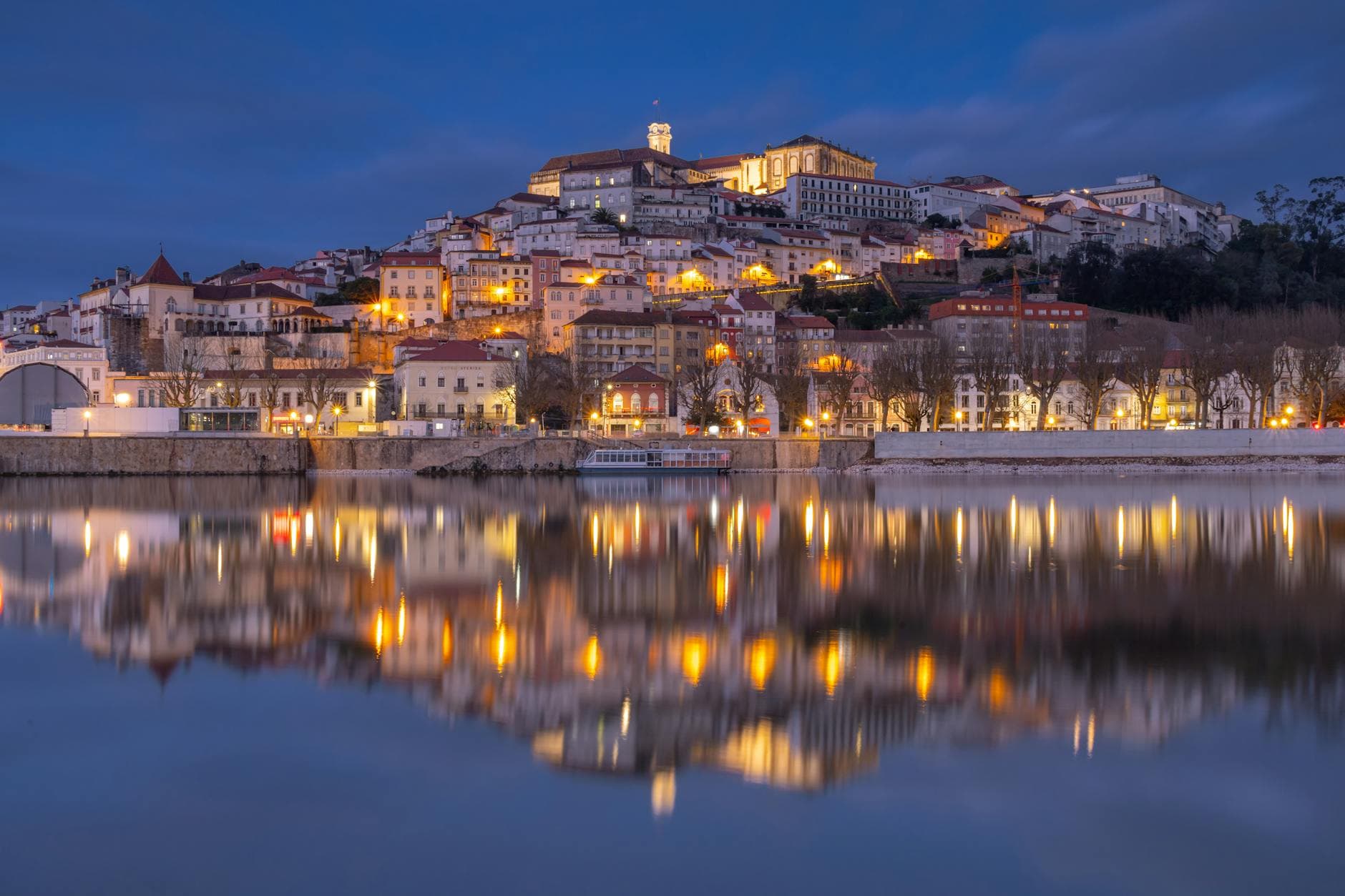 Magical evening view of Coimbra city lights reflecting in the water under a twilight sky.