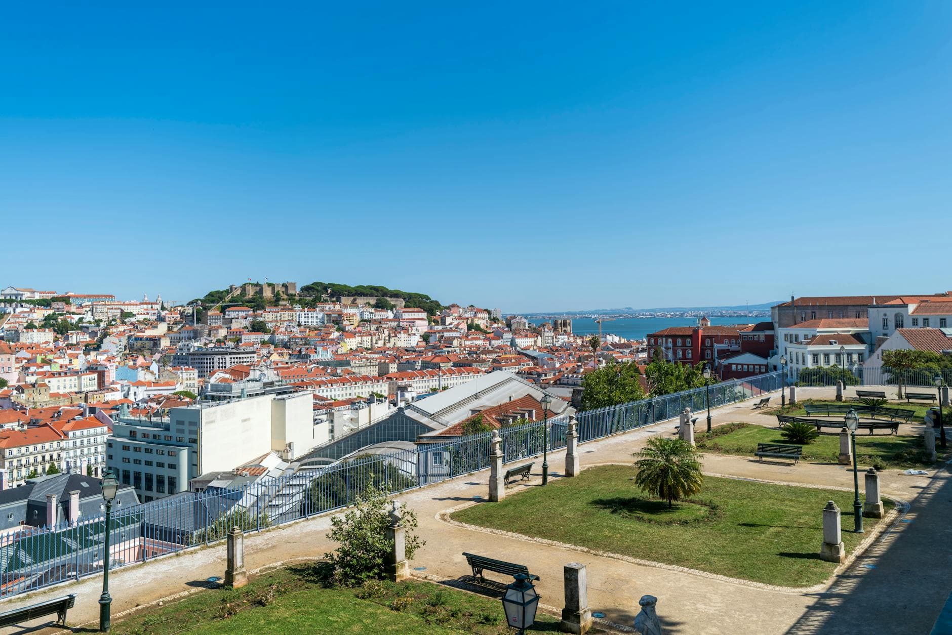 Elevated view of Lisbon skyline and São Jorge Castle under blue skies, from a park.