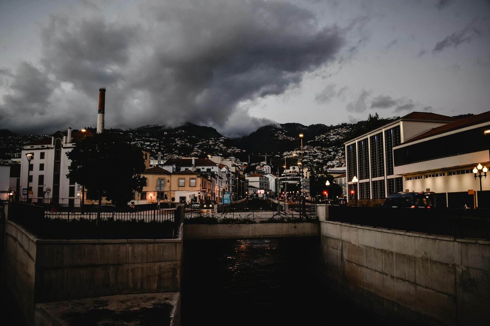Dramatic evening view of Funchal, Madeira with a cloudy sky and city lights illuminating the streets.