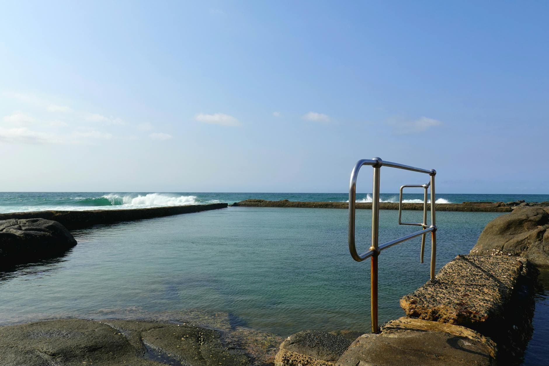 Tranquil coastal rock pool with waves at Ballito, South Africa under a clear blue sky.
