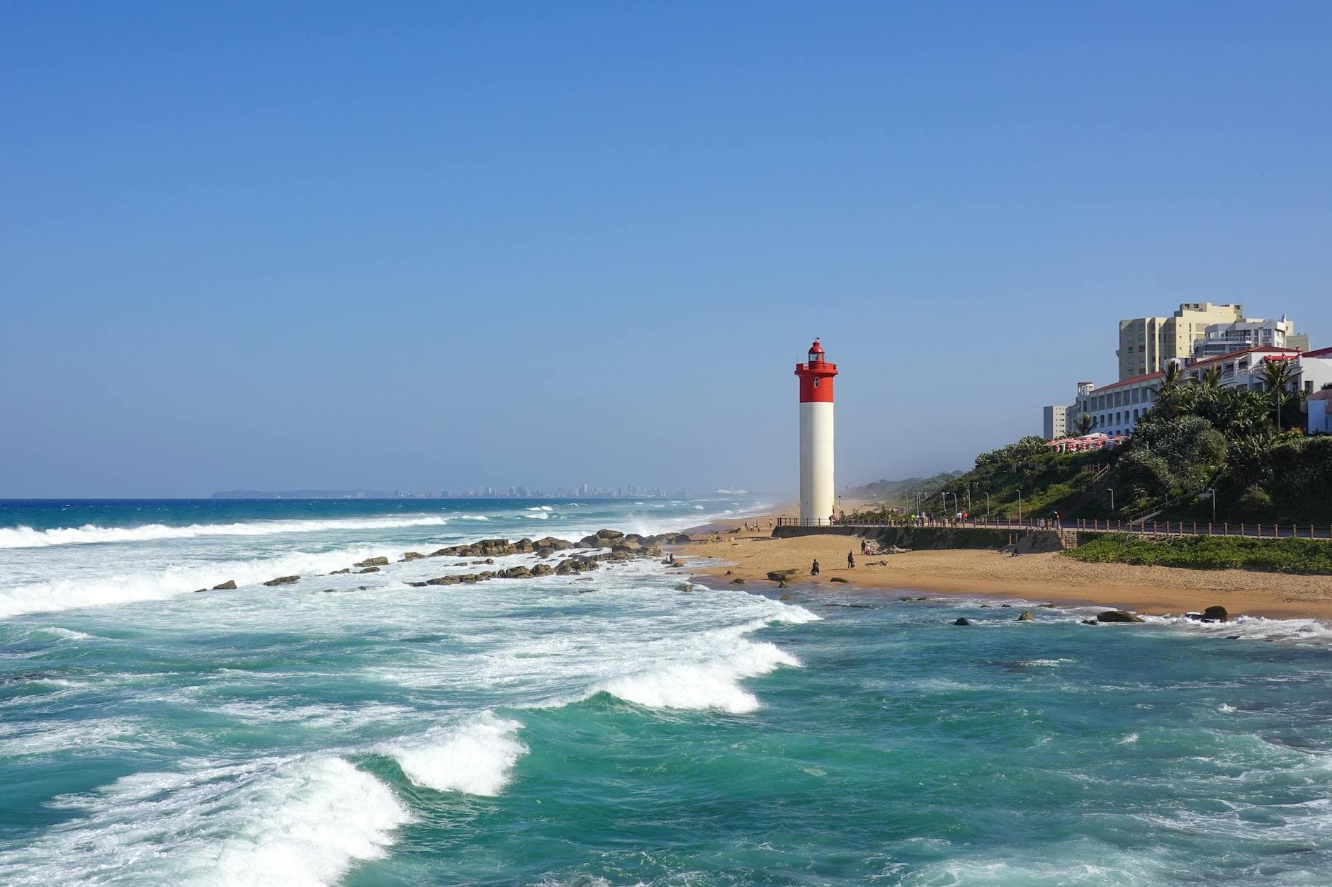 Scenic view of Umhlanga lighthouse and ocean waves under a clear blue sky.