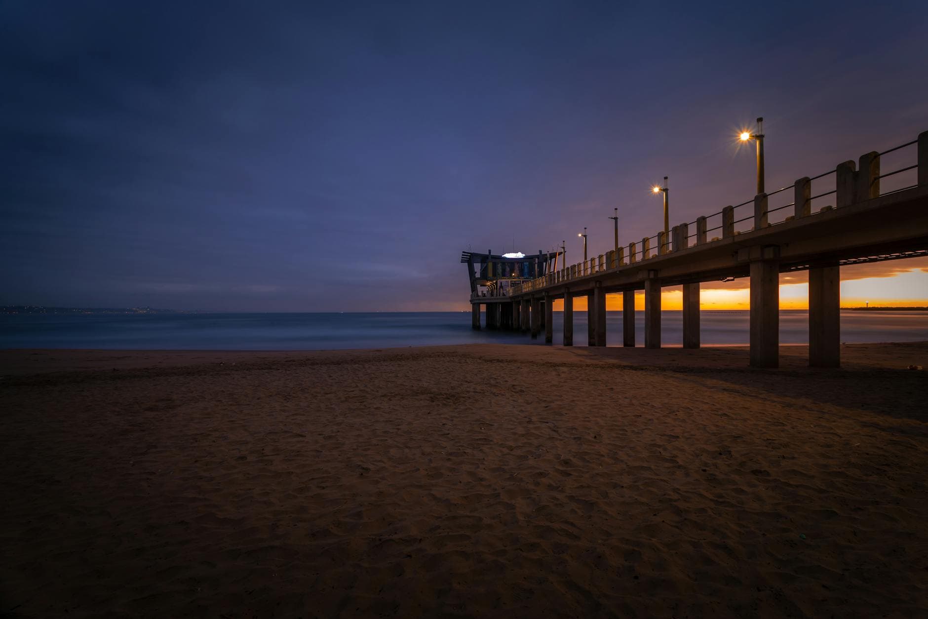 Explore the serene beauty of Durban's iconic pier during sunrise with a calm ocean and sandy beach.