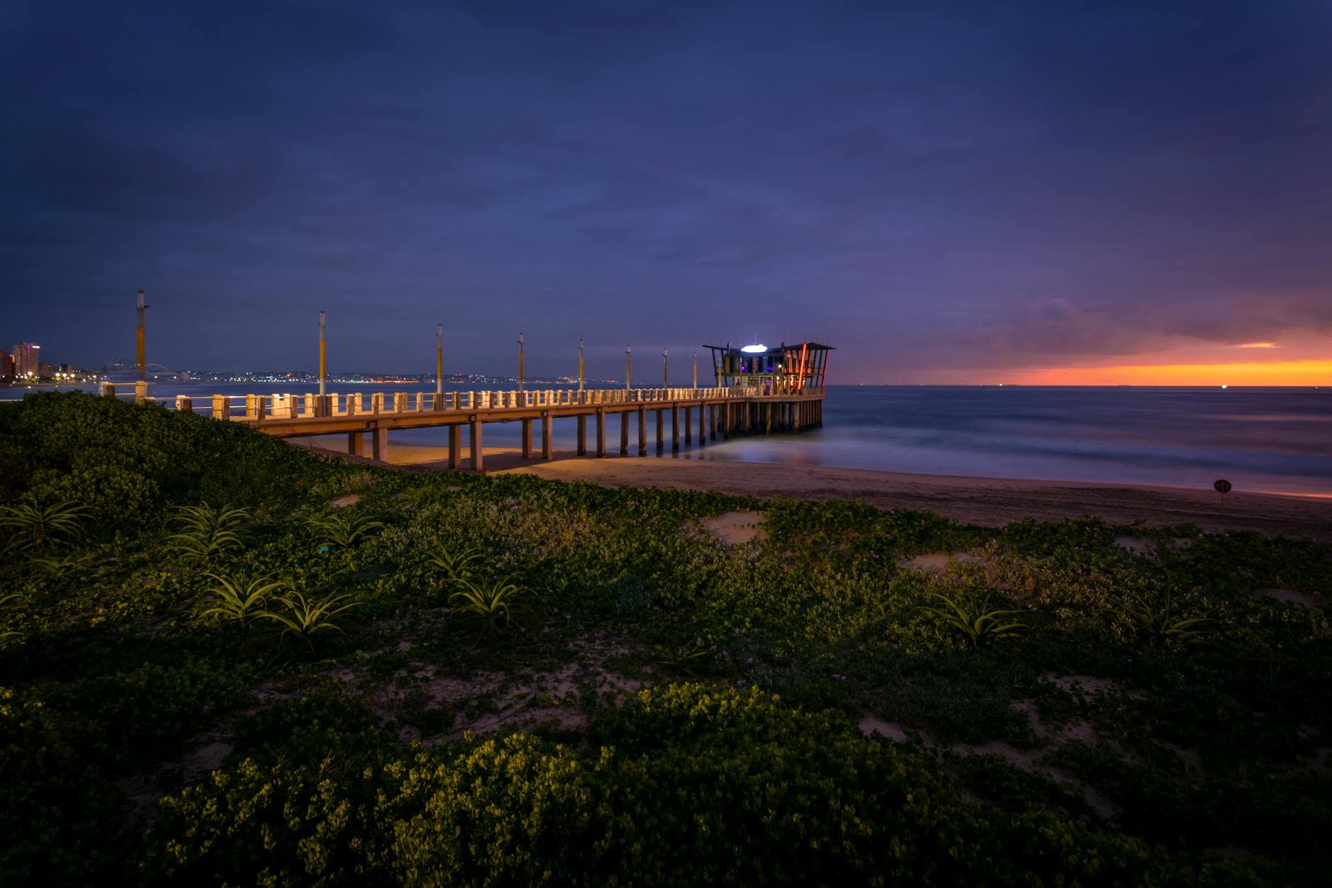 Beautiful sunrise at Durban beach with a vibrant sky, showcasing a picturesque pier and serene ocean.
