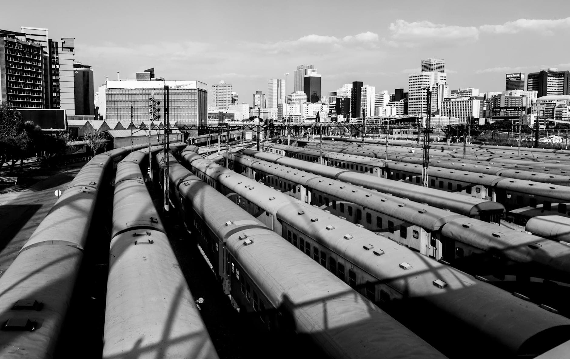 Aerial black and white view of trains in a busy Johannesburg station with cityscape in the background.