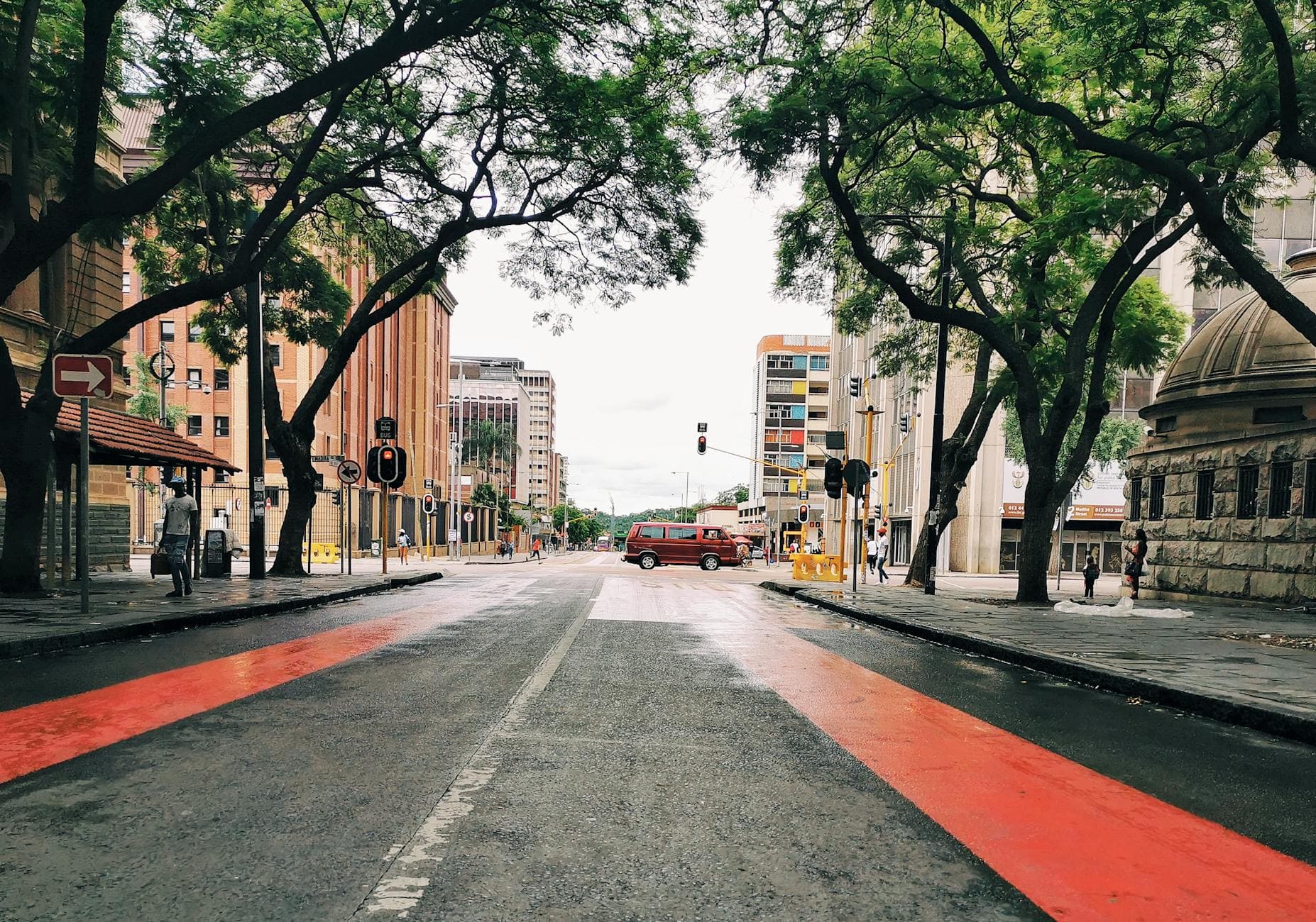 Wet urban street in Pretoria with trees and buildings, showcasing city life.