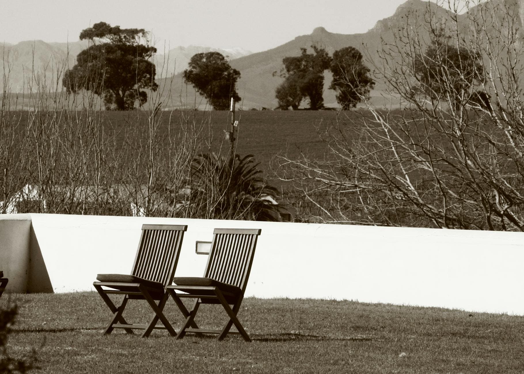Two wooden chairs on a lawn overlooking a serene countryside landscape in Stellenbosch, South Africa.