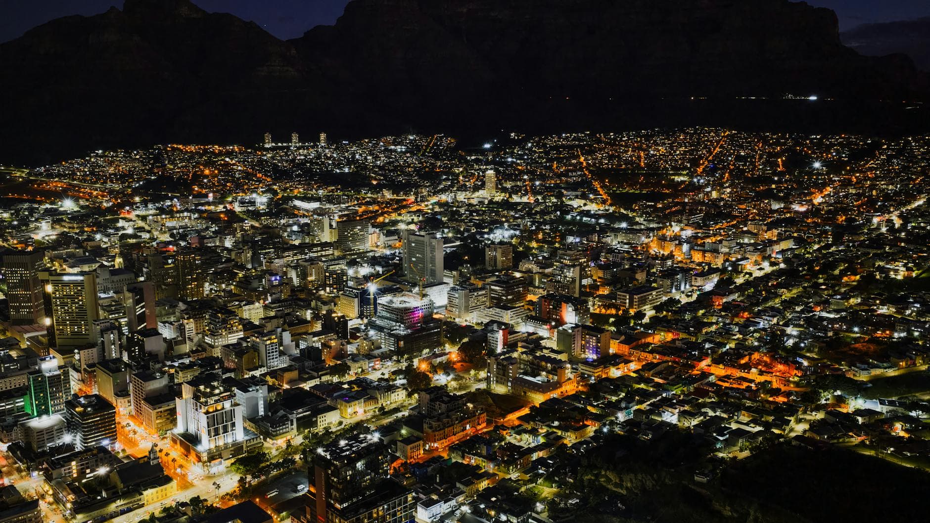 Stunning aerial night view of Cape Town cityscape, showcasing illuminated buildings and streets.