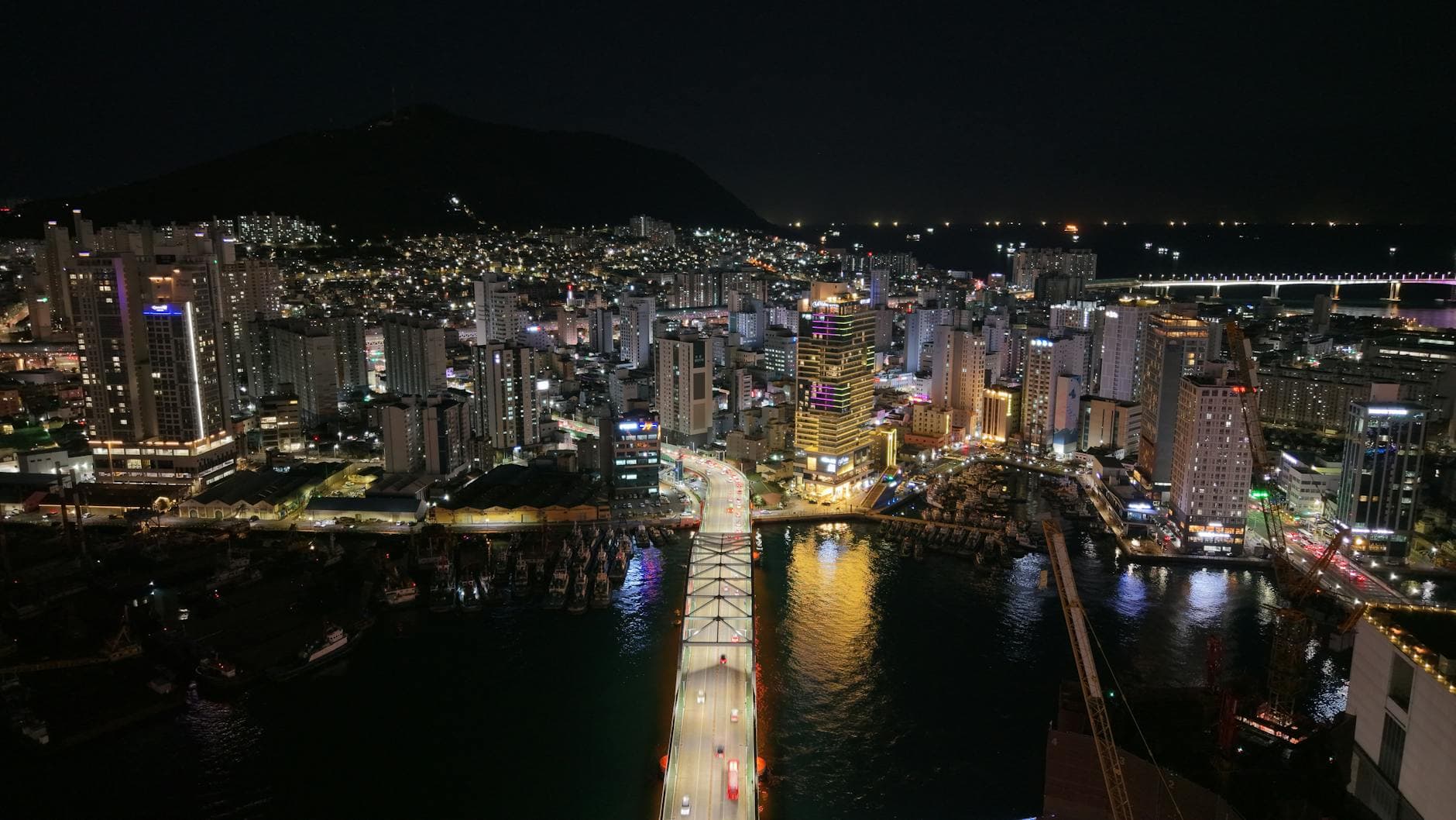 Stunning aerial shot of Busan cityscape at night, featuring illuminated skyscrapers and a bridge.