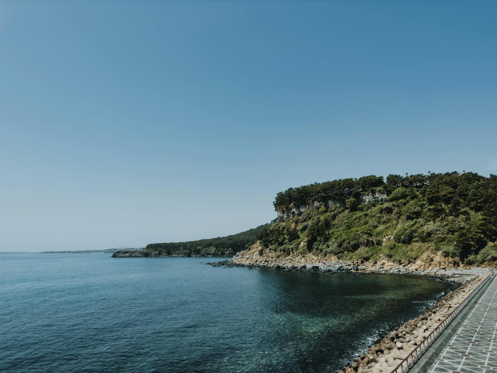 Breathtaking view of Jeju Island's coastline with clear skies and lush greenery.
