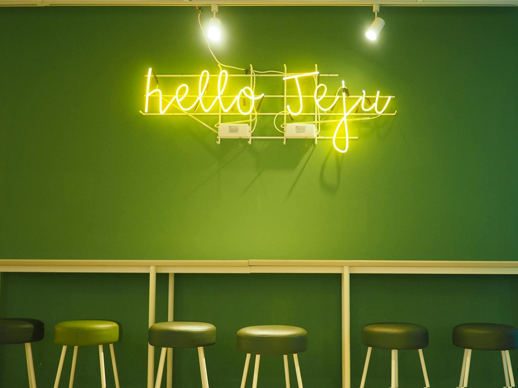 Chic interior with neon 'hello Jeju' sign and green stools against a matching wall.