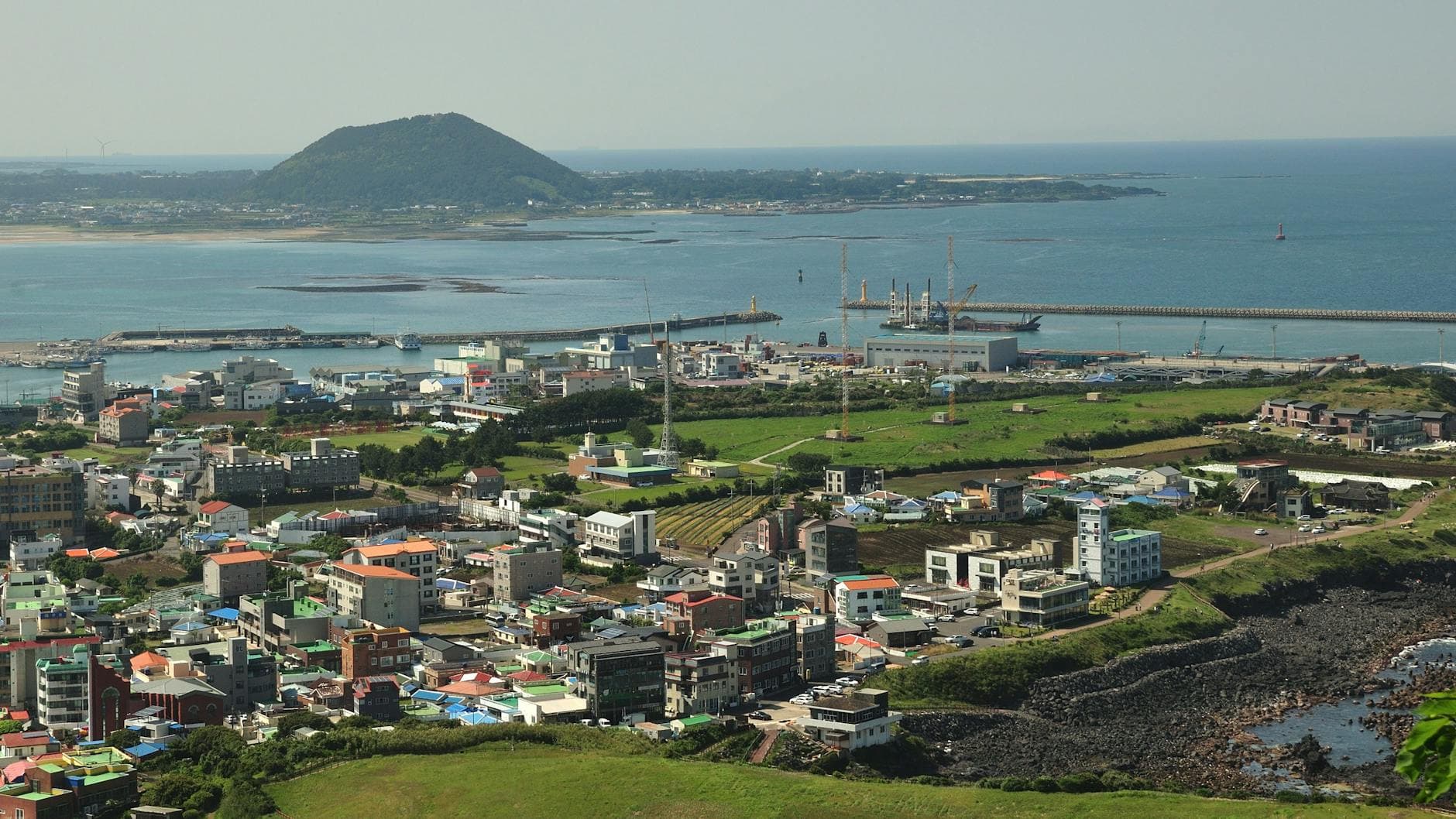 Discover the vibrant coastal cityscape of Jeju Island, featuring lush greenery and modern architecture by the sea.