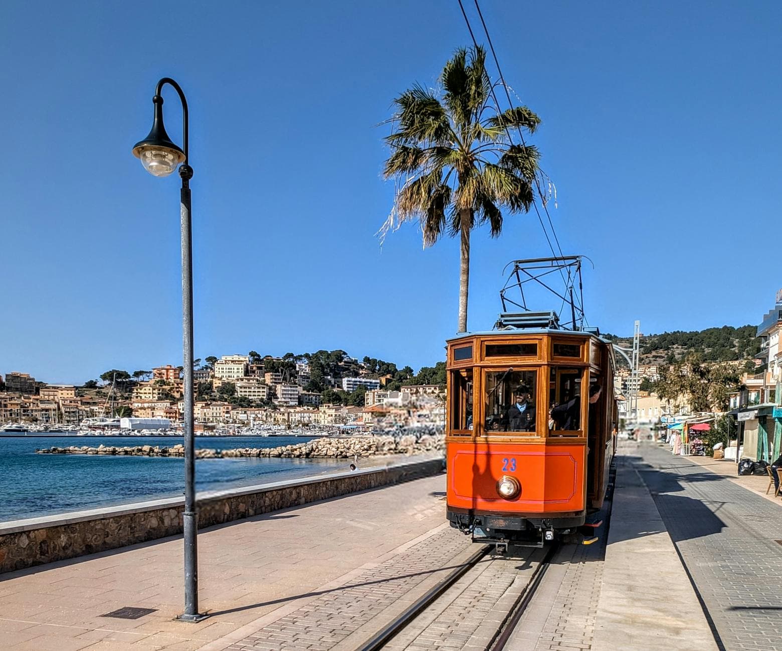 Historic red tram glides along the charming seaside promenade of Sóller, Mallorca, under clear blue skies.