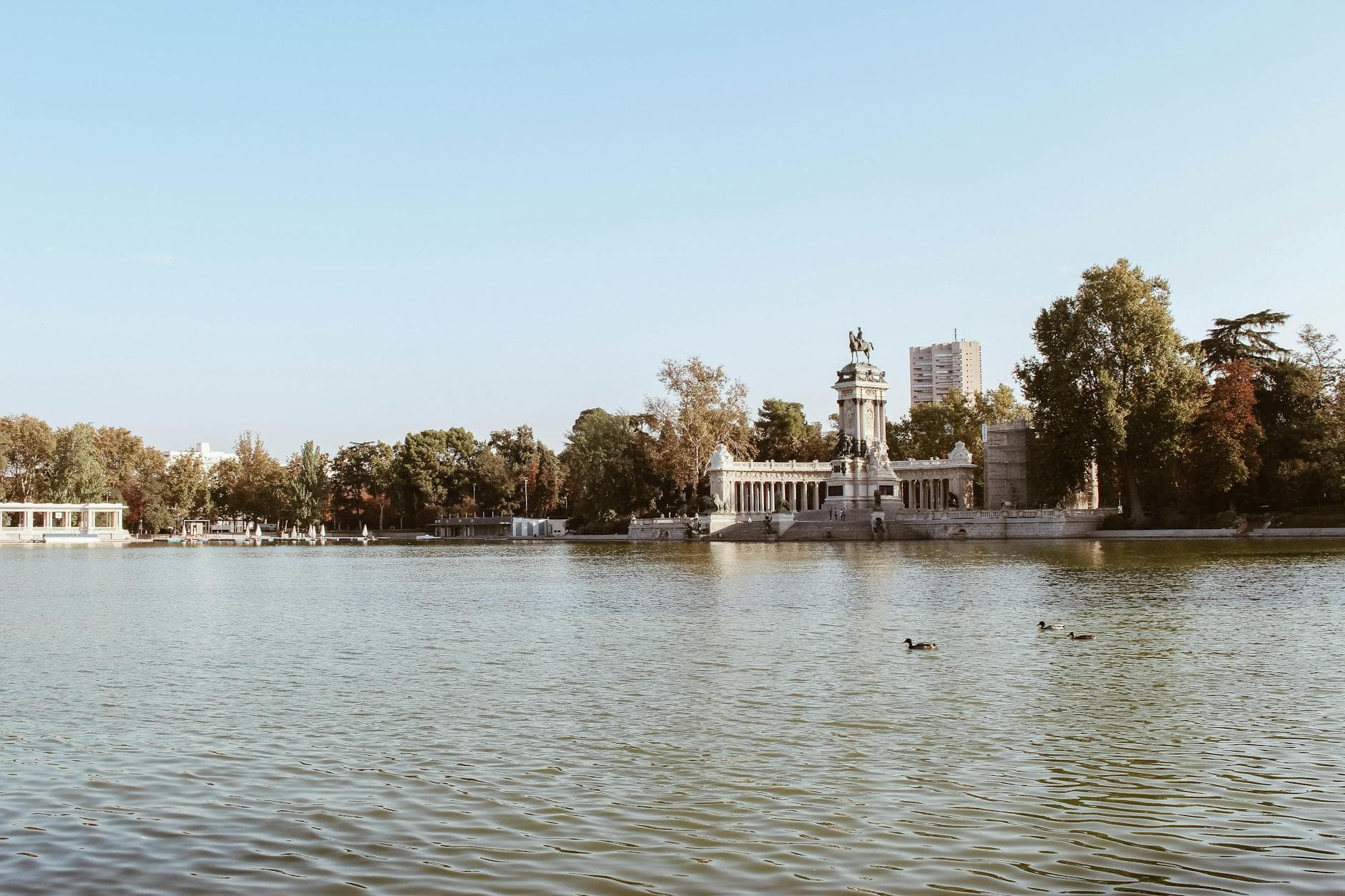View of the monument and lake at El Retiro Park in Madrid, Spain, under a clear blue sky.
