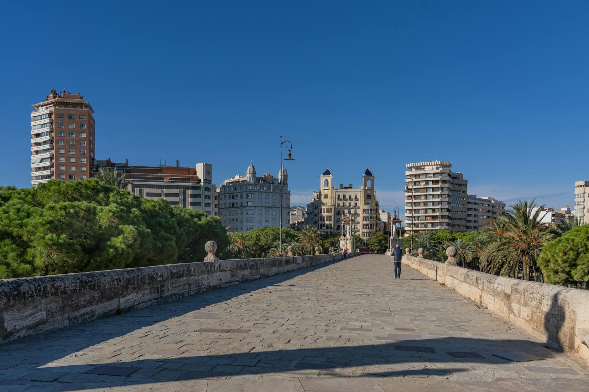 View of Valencia's skyline from a historic stone bridge on a sunny day, with clear blue skies.