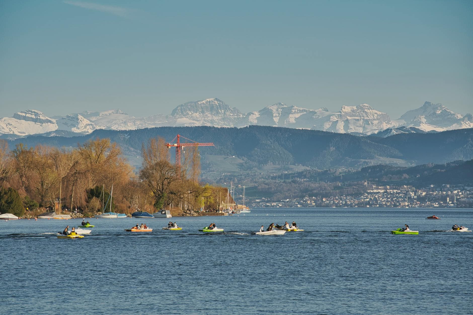 A picturesque view of Lake Zurich with people boating and the snowy Alps in the background.