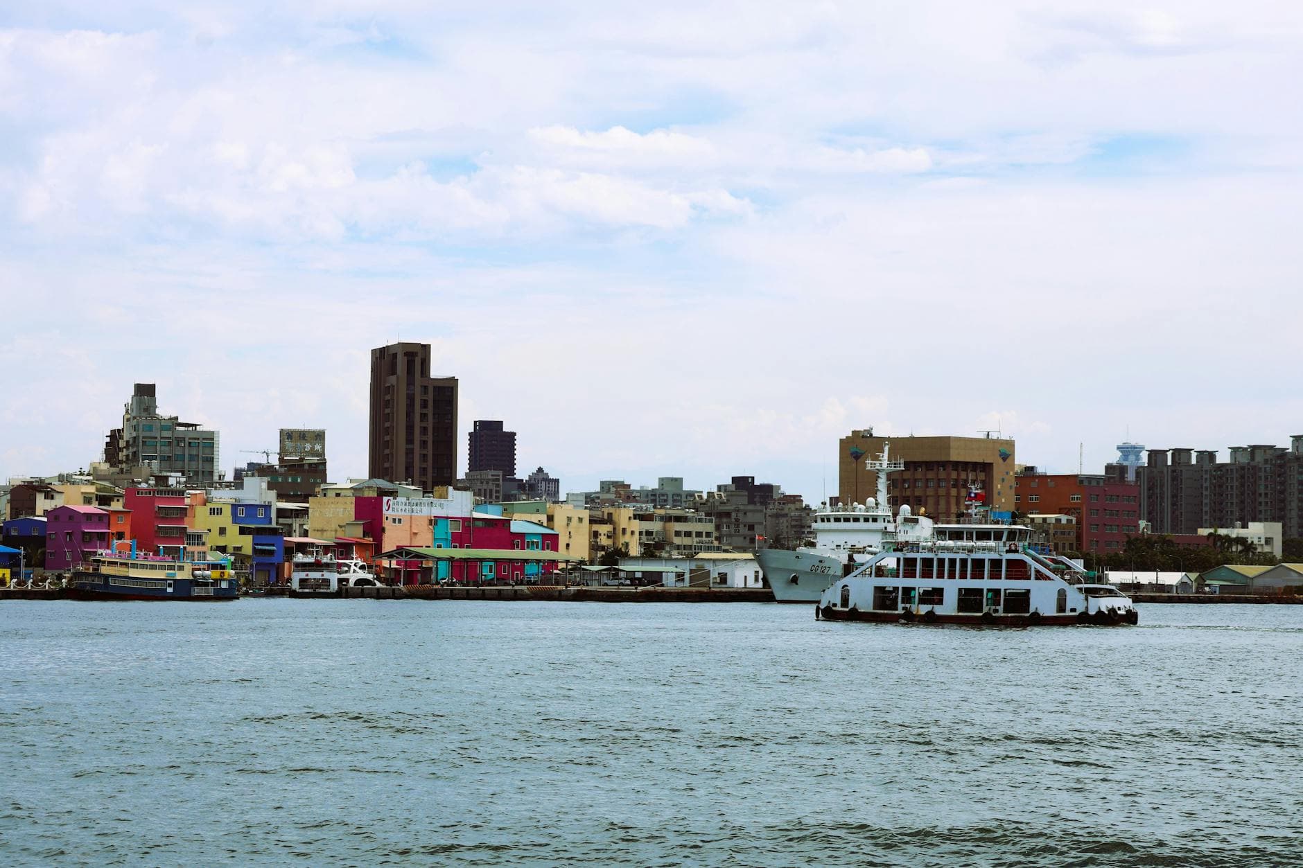 Colorful waterfront view of Kaohsiung, Taiwan with ferry crossing the harbor.