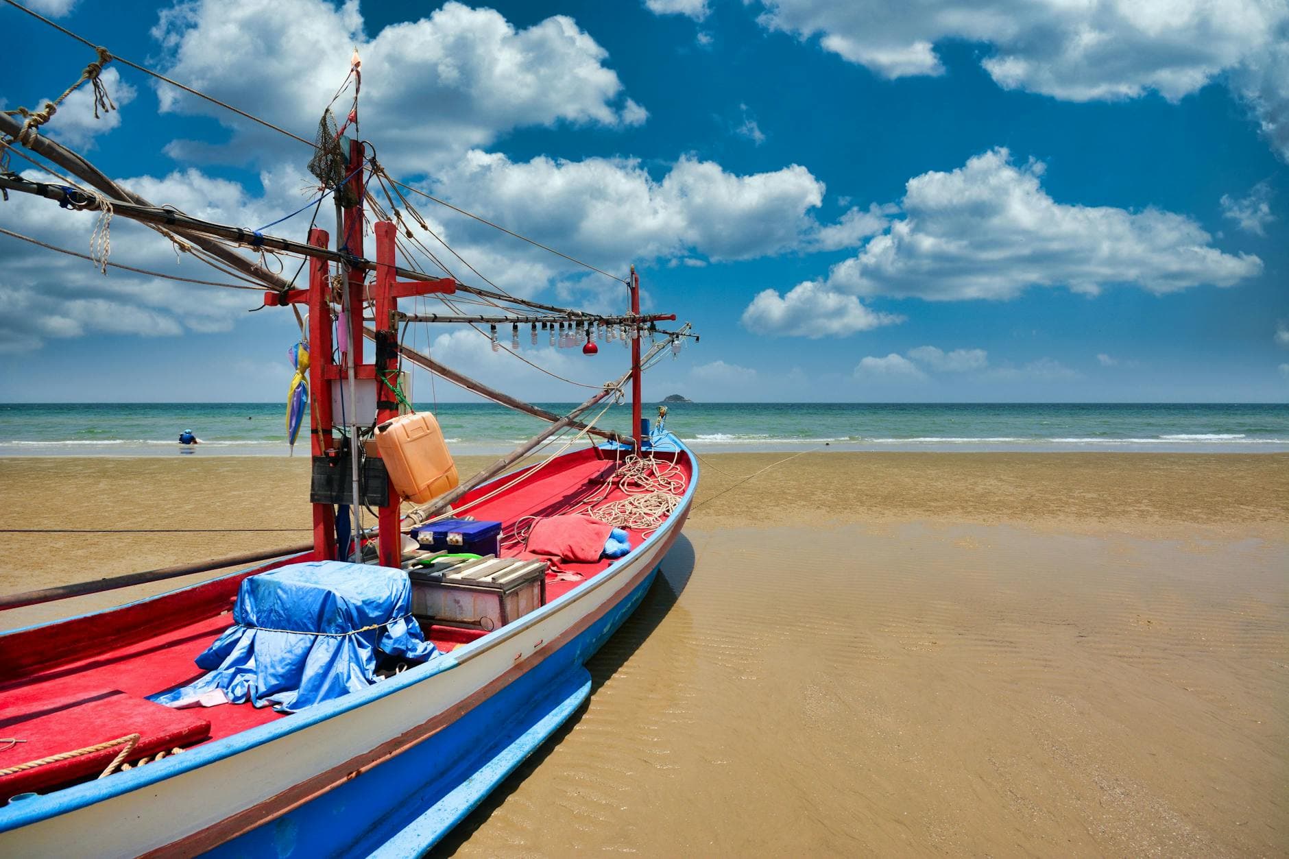 A colorful fishing boat rests on the sandy Hua Hin beach under a bright blue sky.