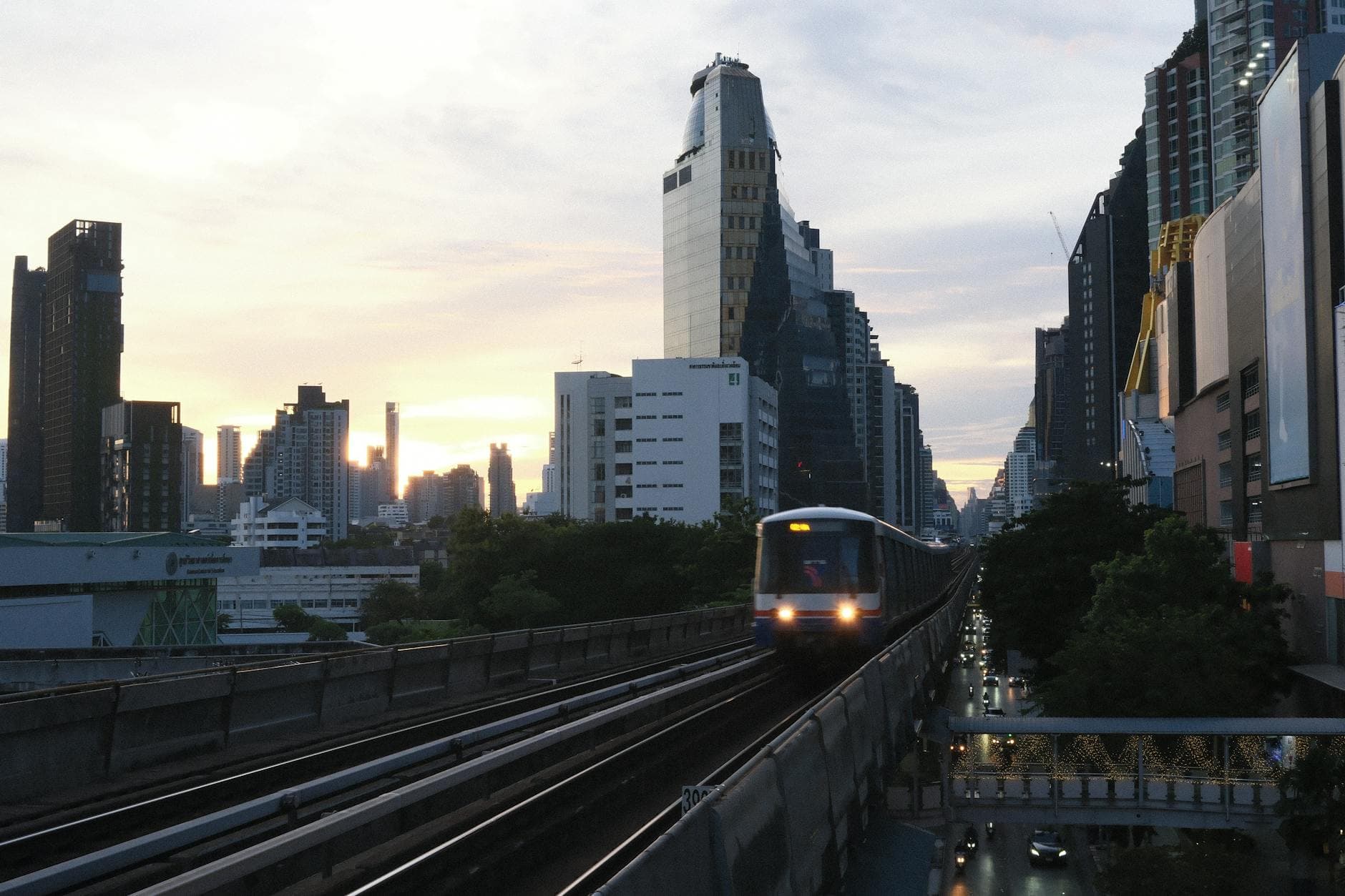 A BTS Skytrain on elevated tracks against the Bangkok skyline during sunset.