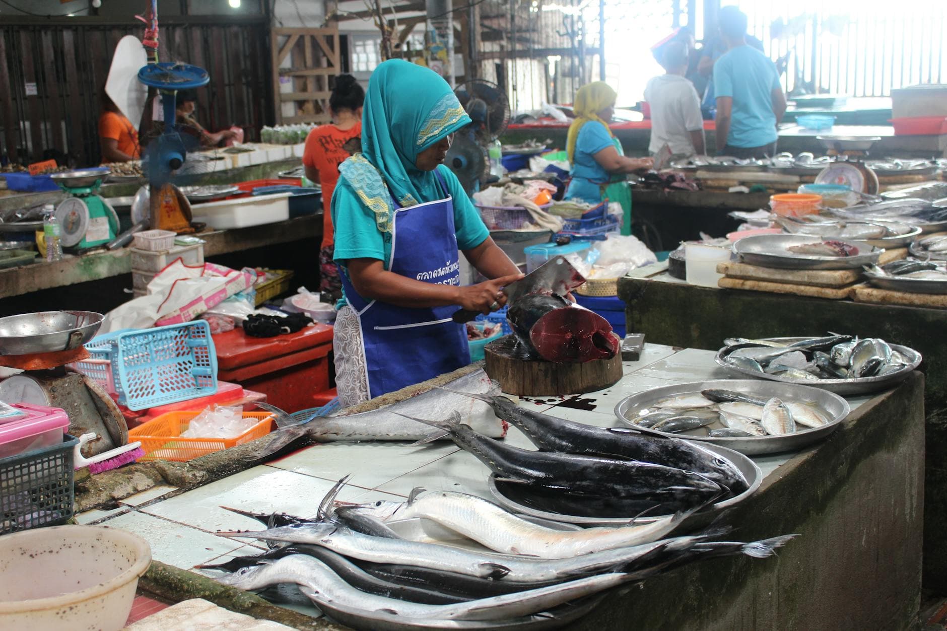 A woman in a headscarf preparing fresh seafood at a wet market in Koh Samui, Thailand.
