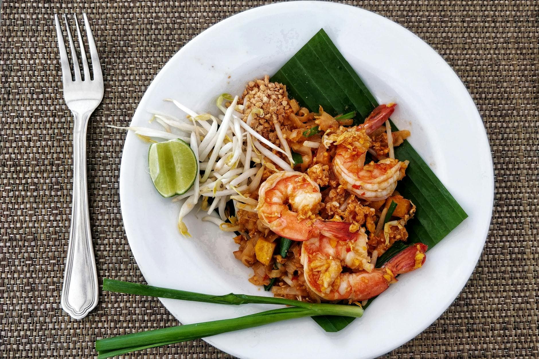 Delicious Pad Thai with shrimps, bean sprouts, and lime on a banana leaf, served on a woven mat.