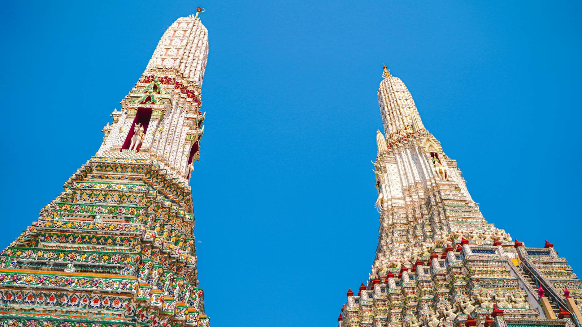 Low angle view of Wat Arun's ornate towers against a clear blue sky in Bangkok, Thailand.