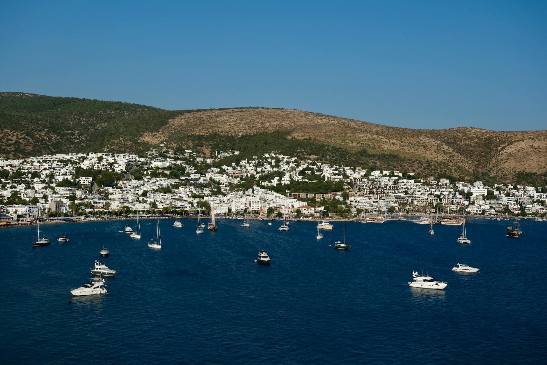 Aerial view of Bodrum harbor, Türkiye, with boats and whitewashed buildings against hills.