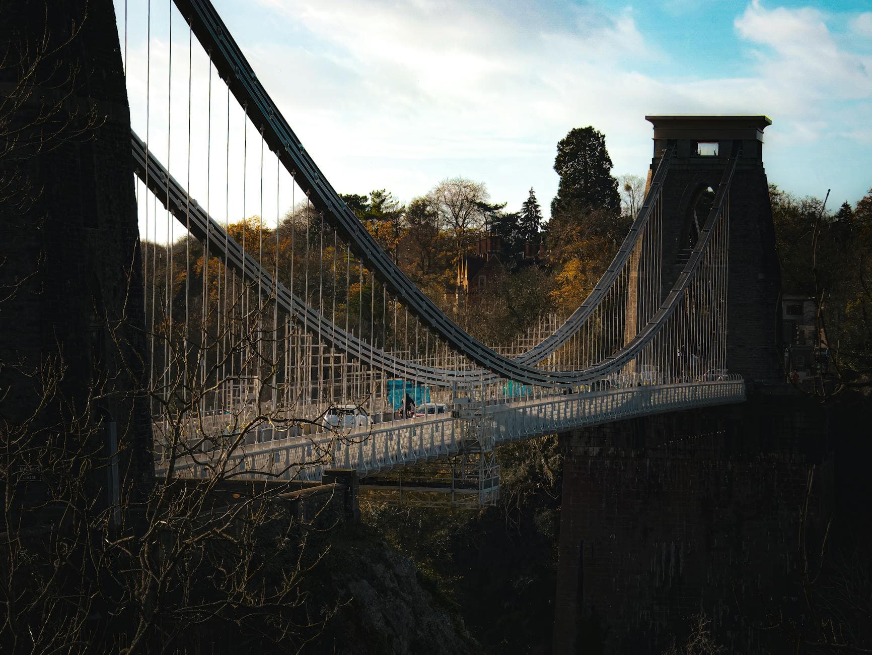 Clifton Suspension Bridge spanning Avon Gorge in fall, under a bright sky.