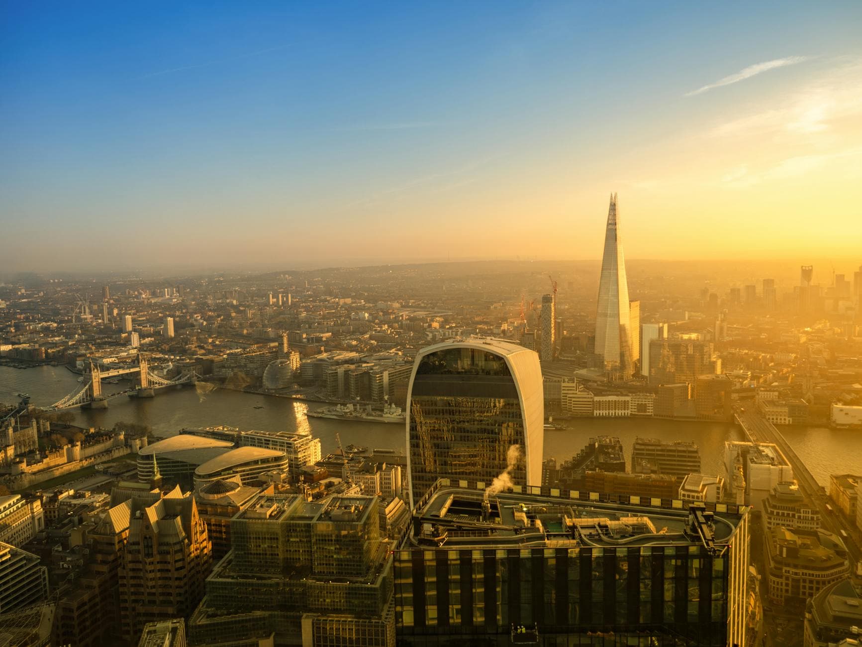 A breathtaking aerial view of London's skyline featuring the Shard and Tower Bridge during sunset.