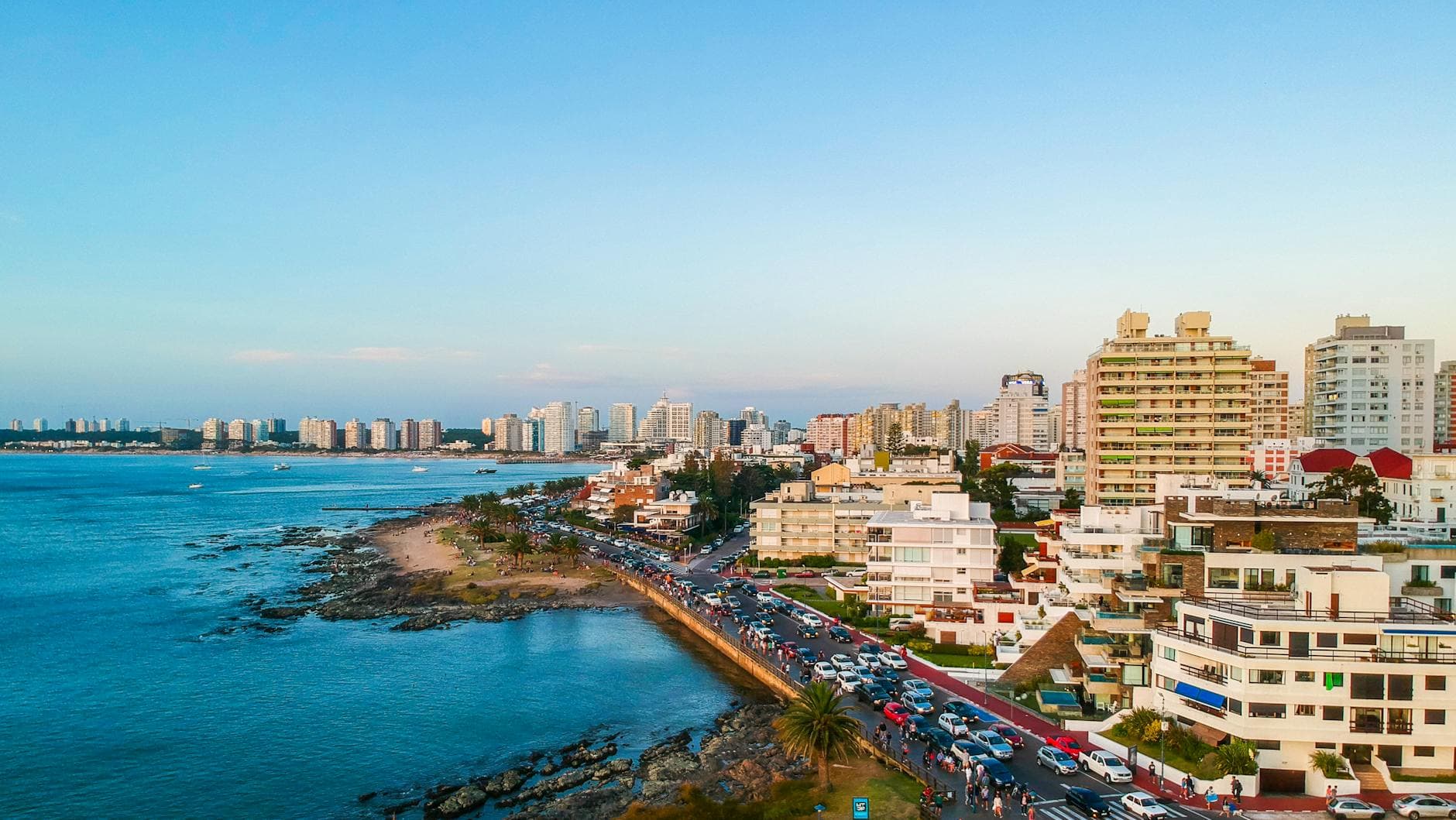 Drone view of ocean shoreline with busy highway and contemporary buildings in sunlight
