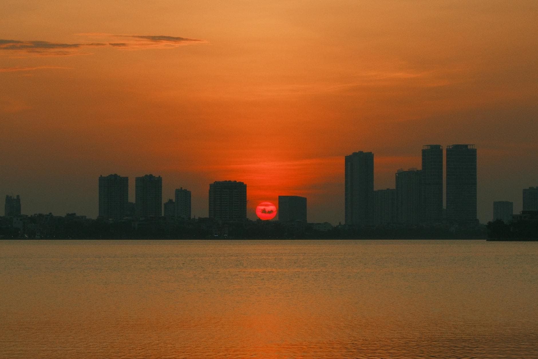 Breathtaking sunset over Hanoi's skyline reflecting on tranquil water with vivid orange hues.