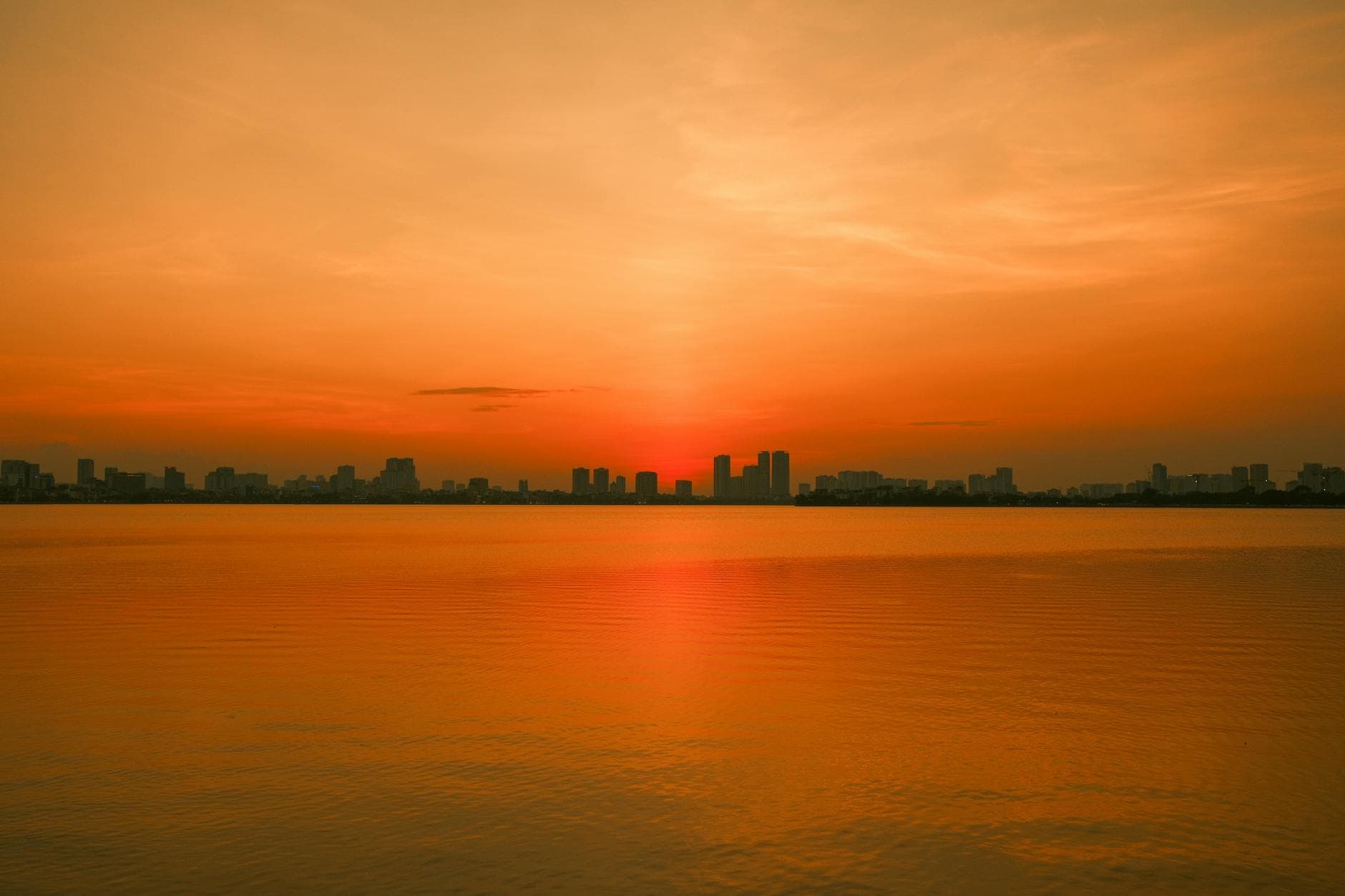 A vivid sunset casts a golden hue over the serene waters of Hanoi, Vietnam.