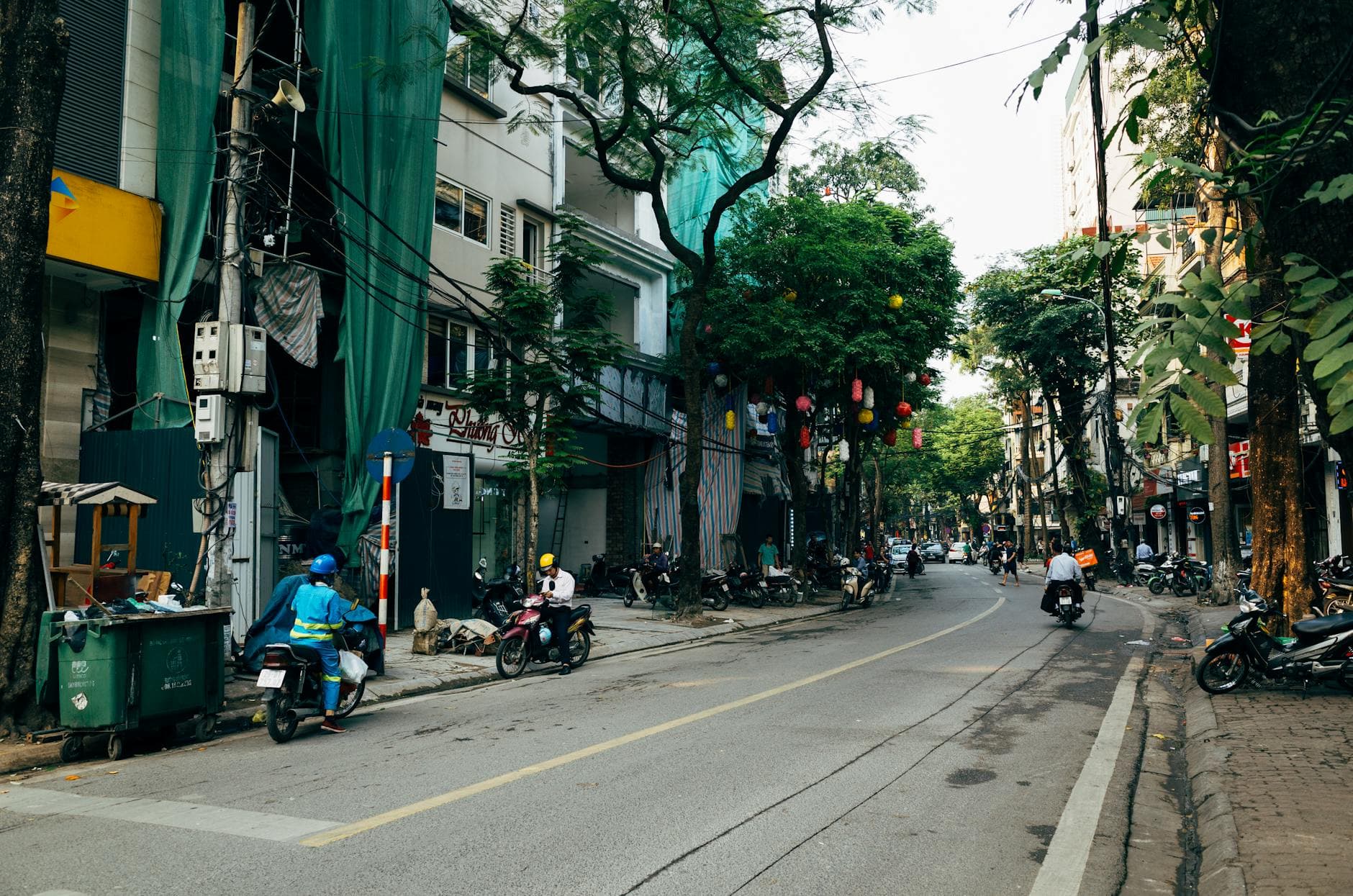 Vibrant Hanoi street scene with motorbikes, trees, and urban life in Vietnam.